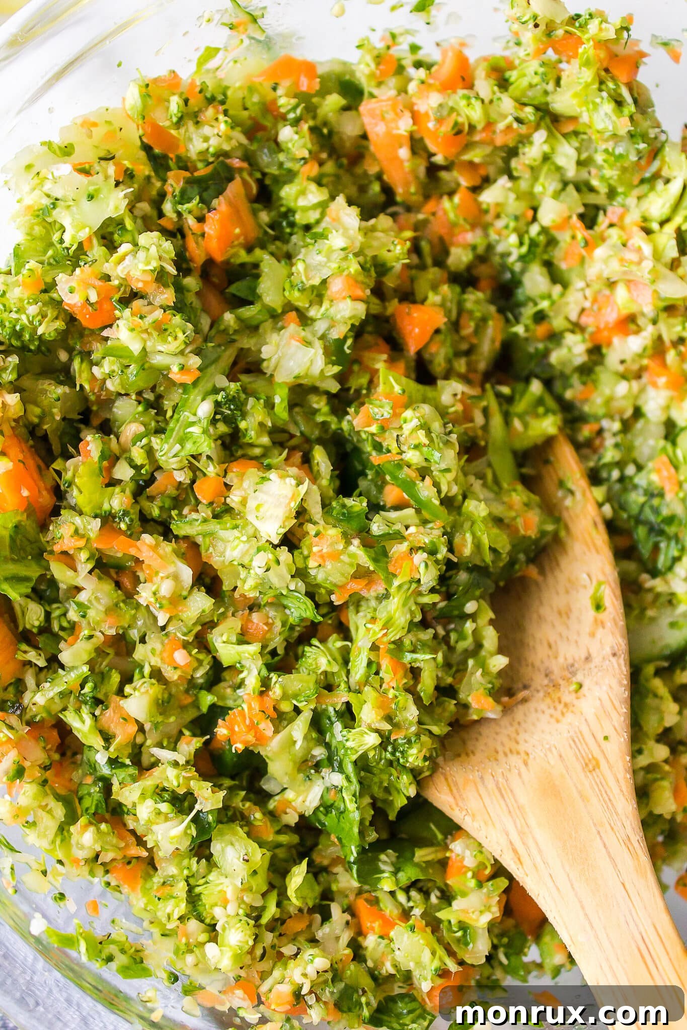 Chopped veggies salad in a glass bowl with a wooden spoon.