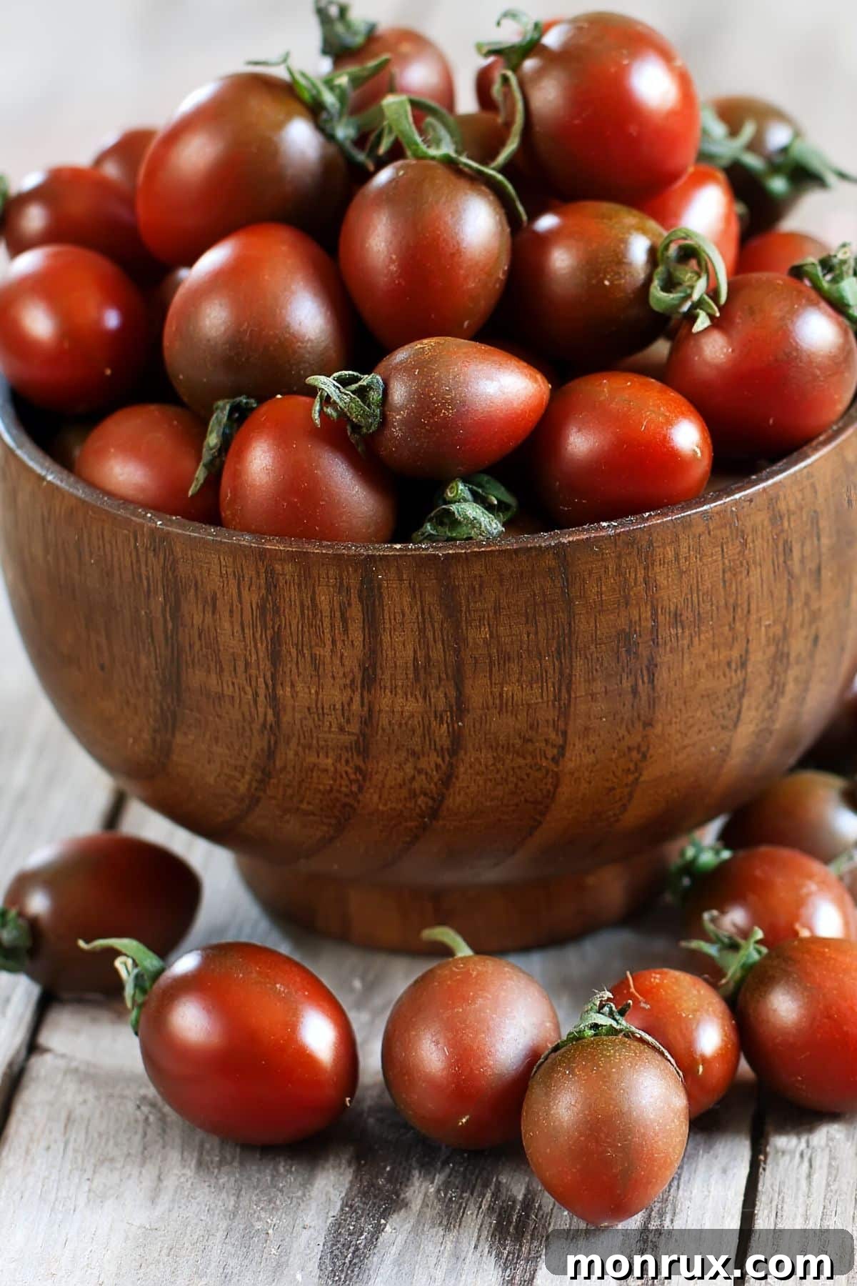 A beautiful wooden bowl brimming with bright red and yellow cherry tomatoes, showcasing their fresh appeal.