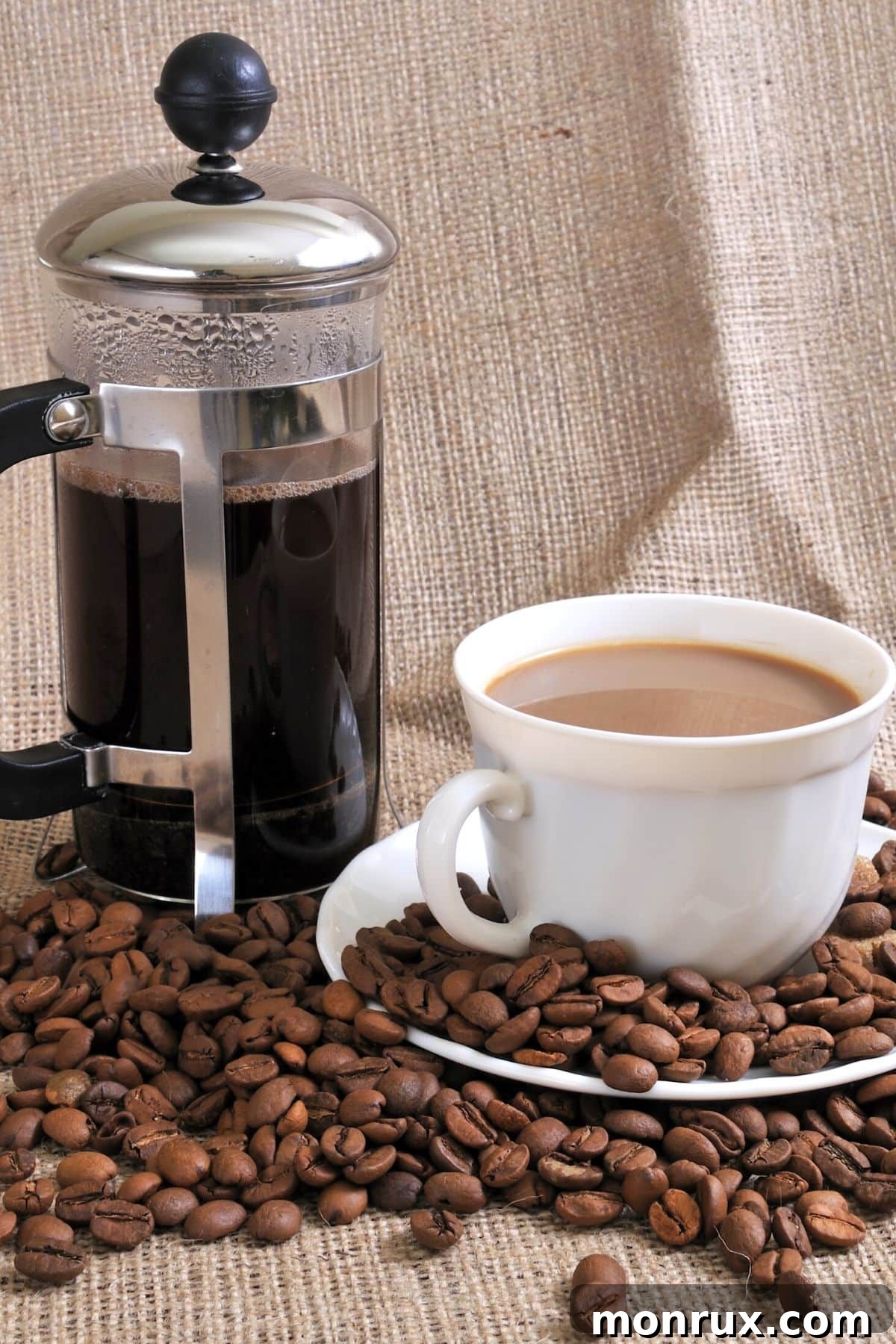 A beautifully set French press and a cup of freshly brewed coffee, surrounded by coffee beans, evoking a sense of rich flavor and morning ritual.