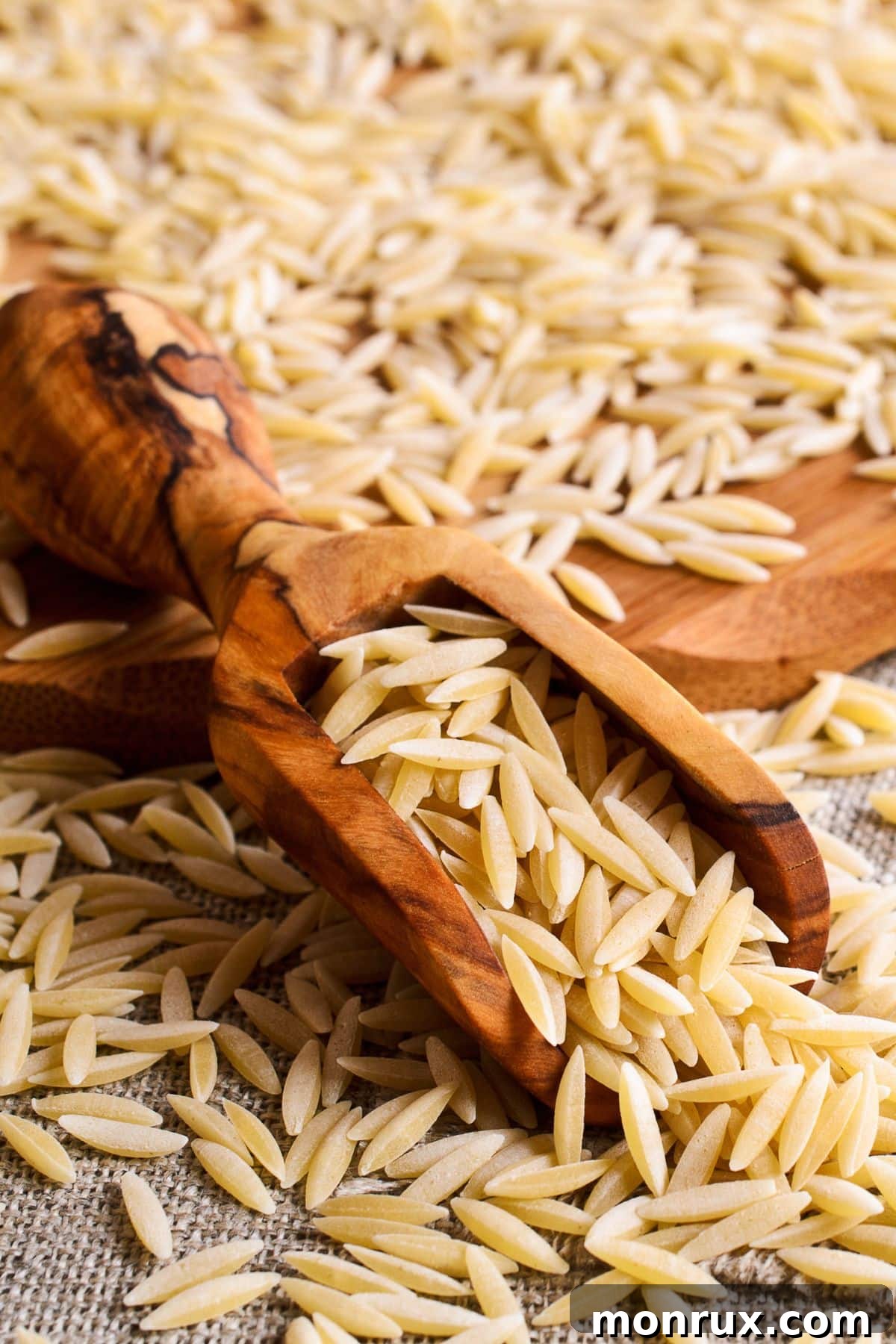 Scoop of orzo pasta on cutting board and burlap. 
