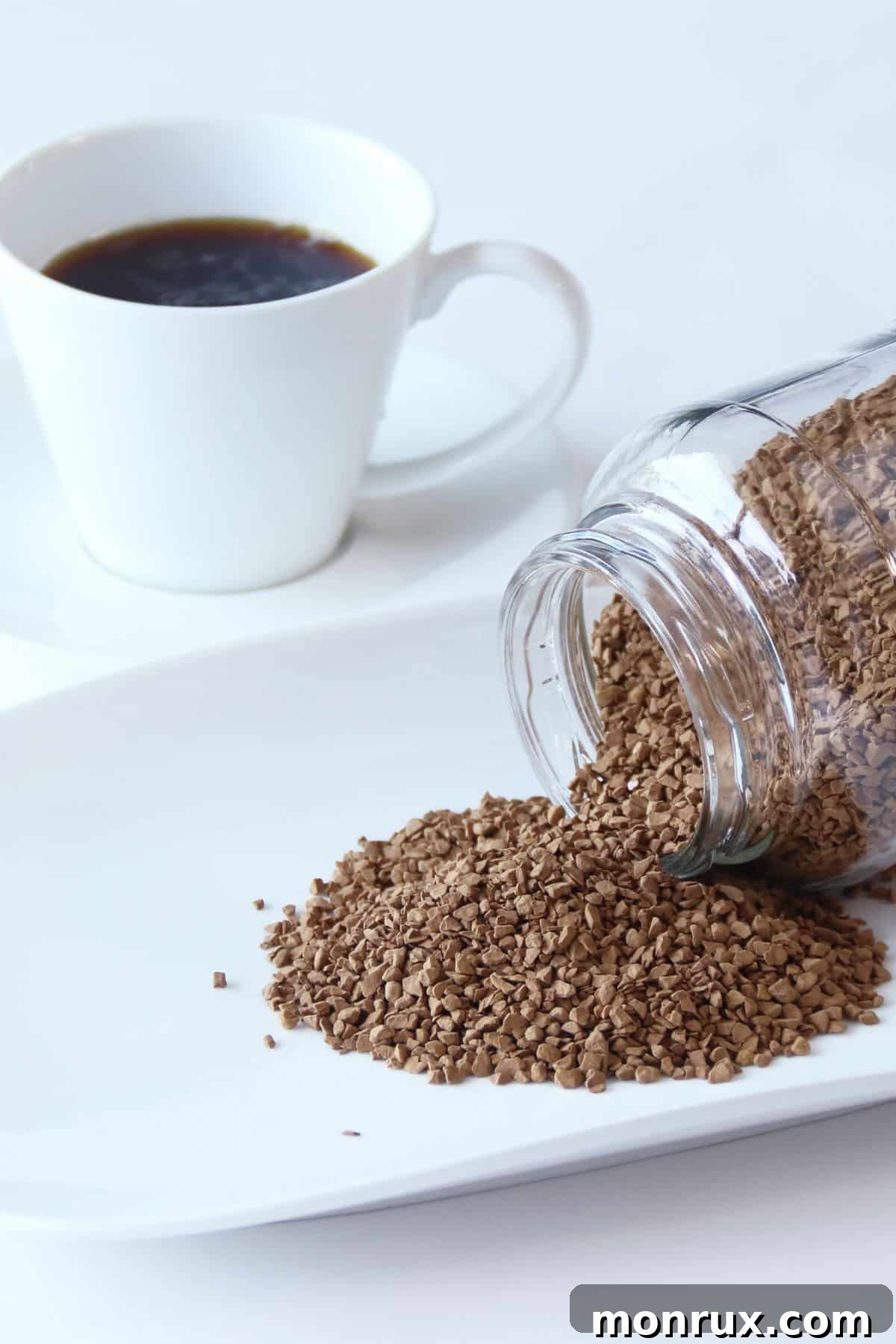 A jar of instant decaf coffee pouring out onto a white plate, showcasing its rich brown granules.