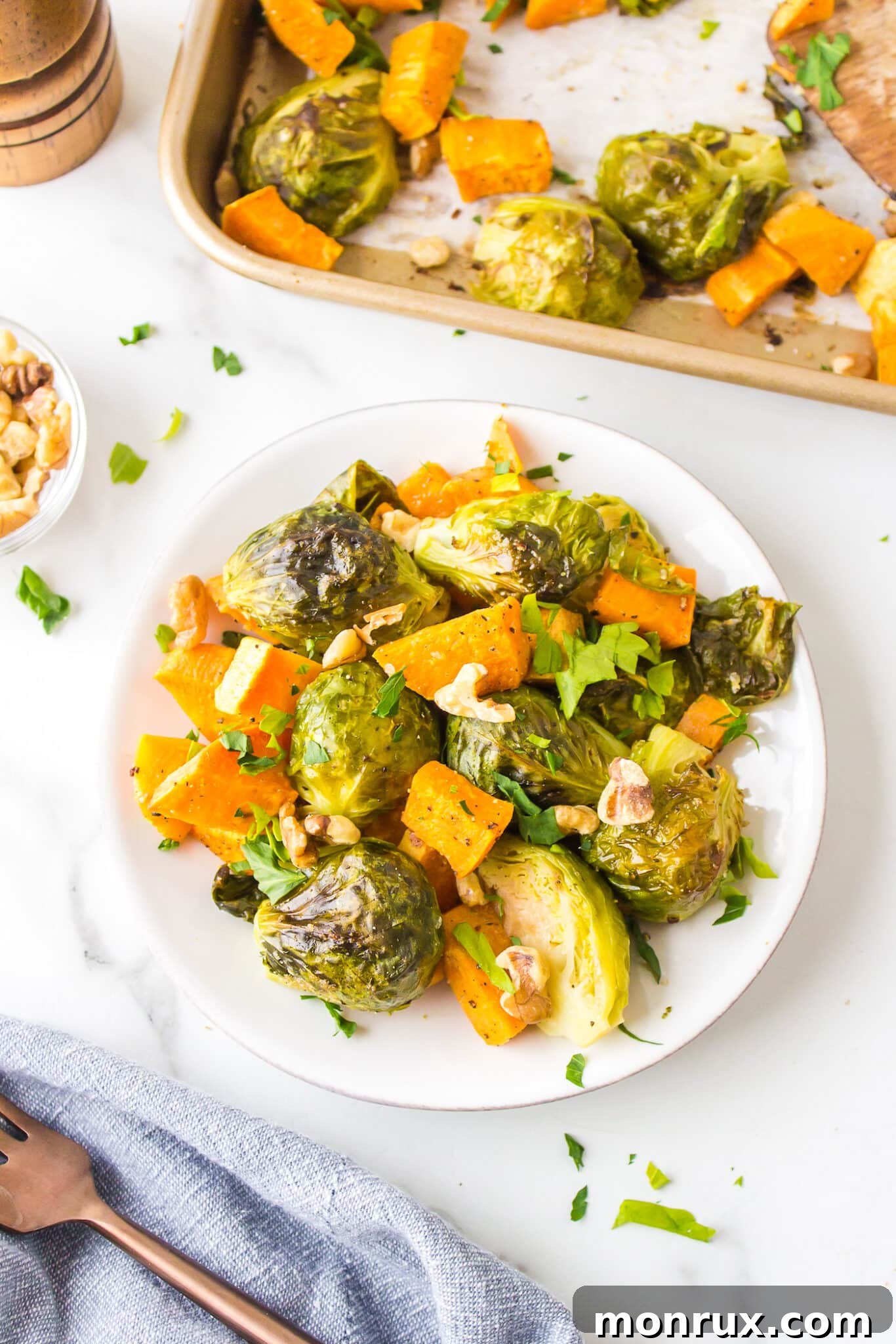 Roasted brussels sprouts and sweet potatoes on a white plate, garnished with fresh herbs.