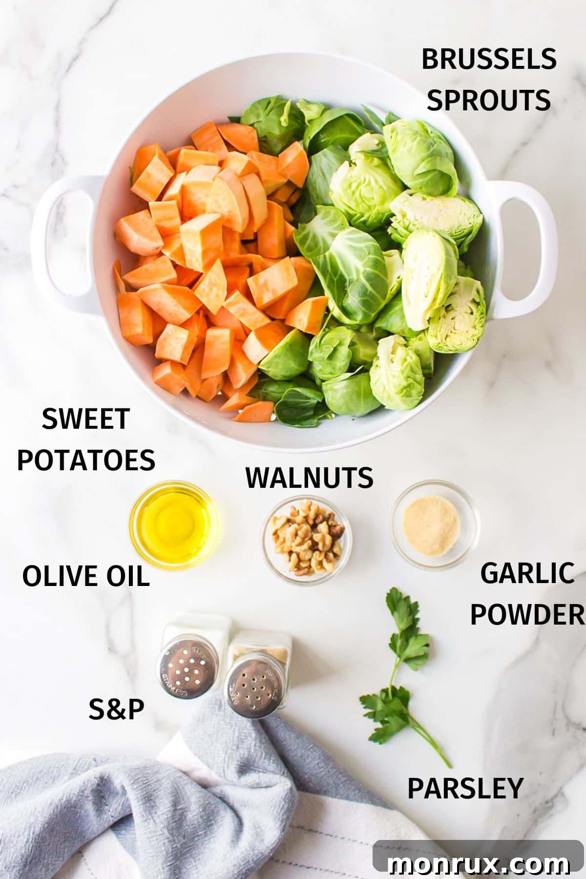 Fresh ingredients laid out on a white background: Brussels sprouts, sweet potatoes, olive oil, garlic powder, salt, pepper, walnuts, and parsley.