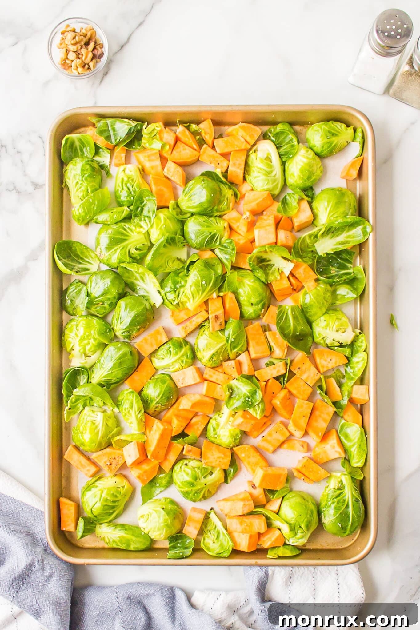 Seasoned Brussels sprouts and sweet potatoes spread on a parchment-lined baking sheet.
