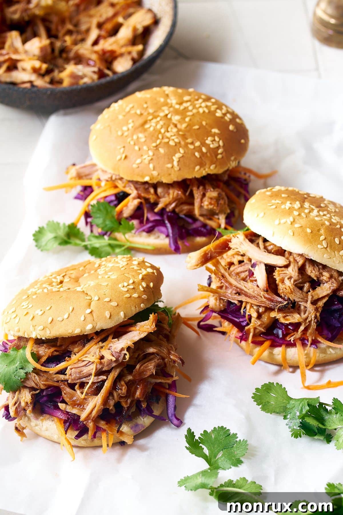 Pulled pork sandwiches with coleslaw and pickles on a white surface, showcasing the versatility of pulled pork.