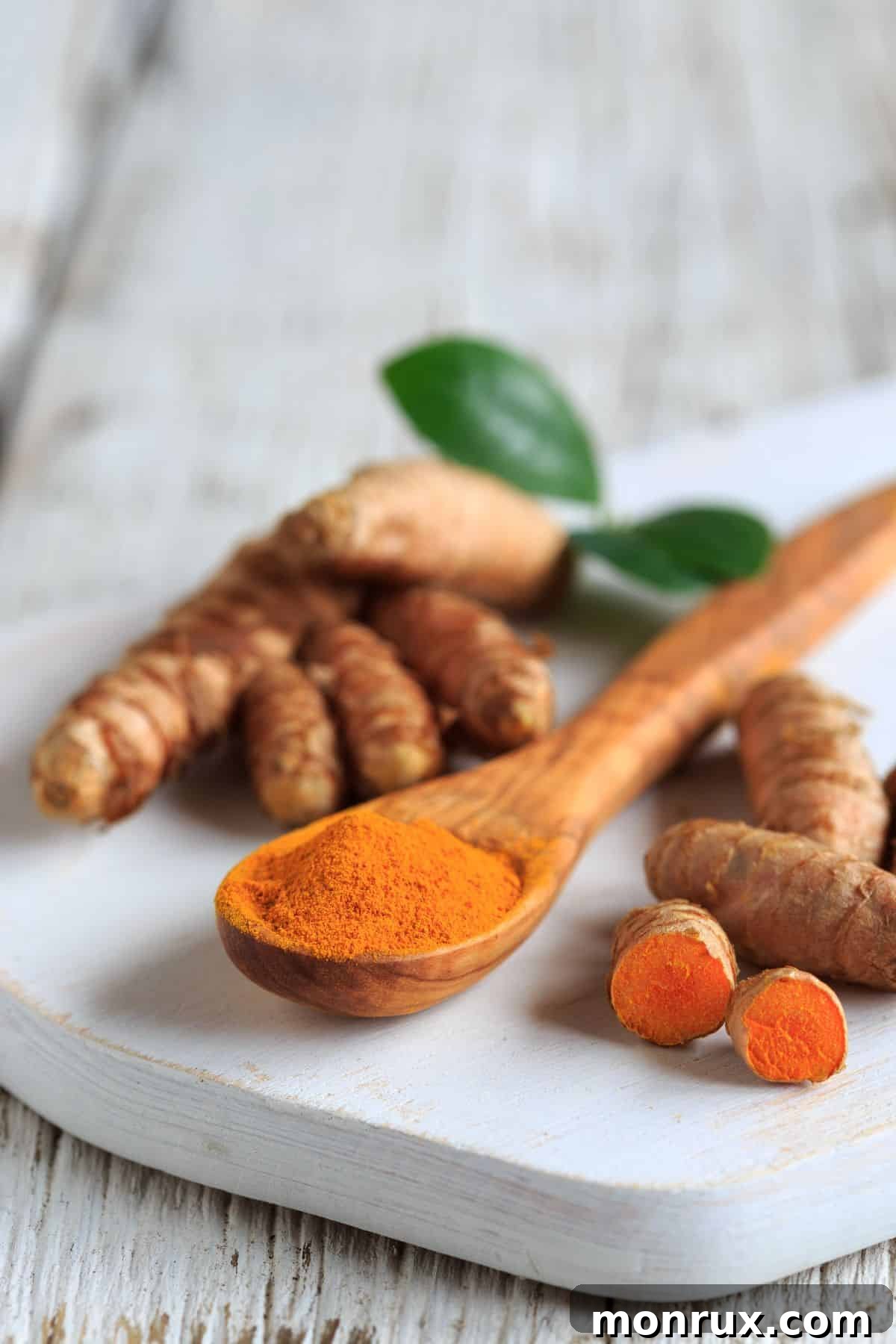 A spoonful of bright yellow turmeric powder next to a piece of fresh turmeric root on a rustic wooden surface.