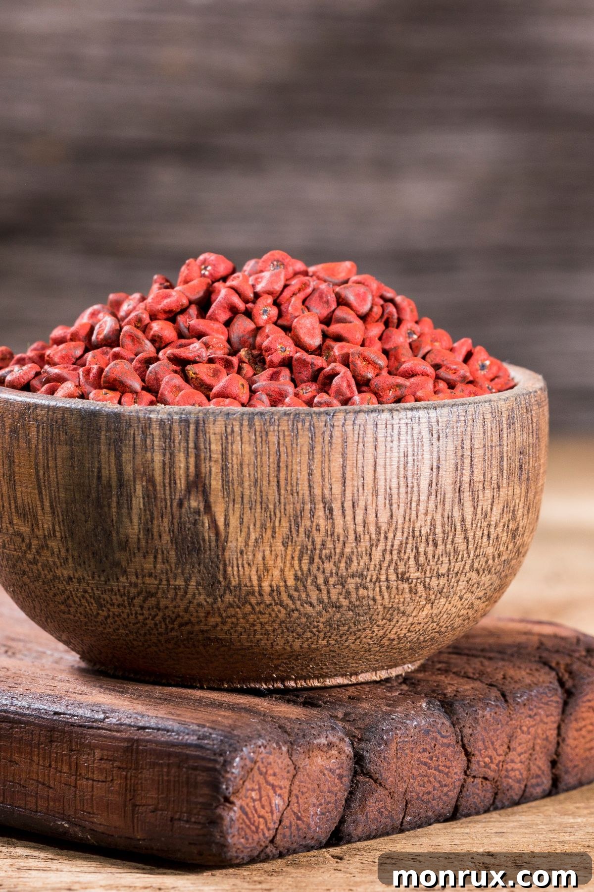 A small wooden bowl filled with bright red-orange annatto seeds, sitting on a natural background.
