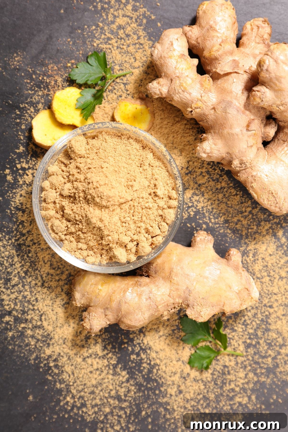 A bowl of light brown ginger powder next to a knotty piece of raw ginger root, set on a rustic wooden surface.