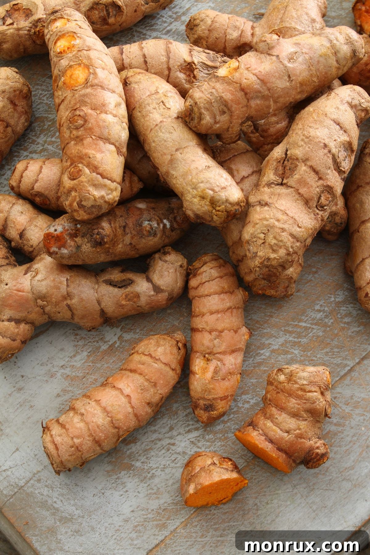 Several pieces of fresh, vibrant orange turmeric root laid out on a dark wooden surface.