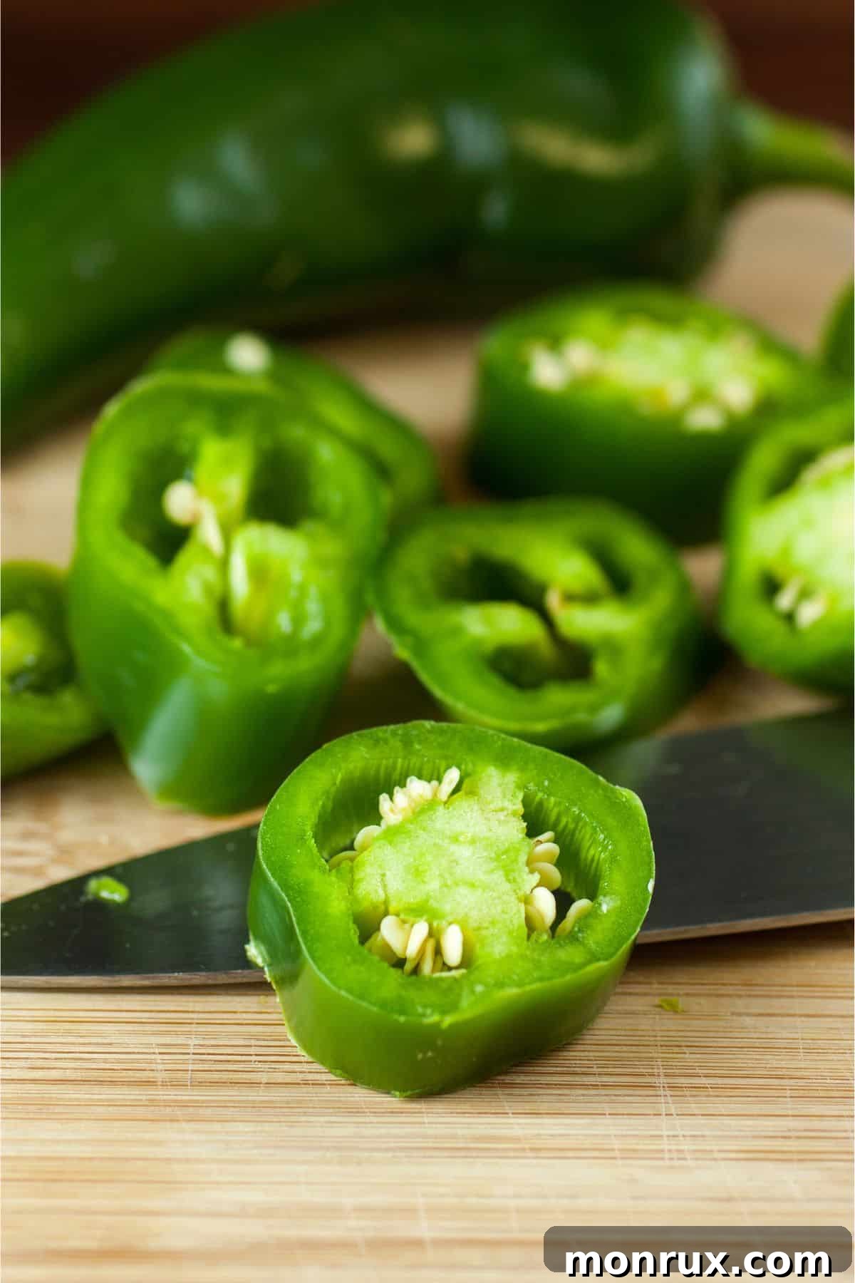 Sliced and whole jalapenos on wooden surface.