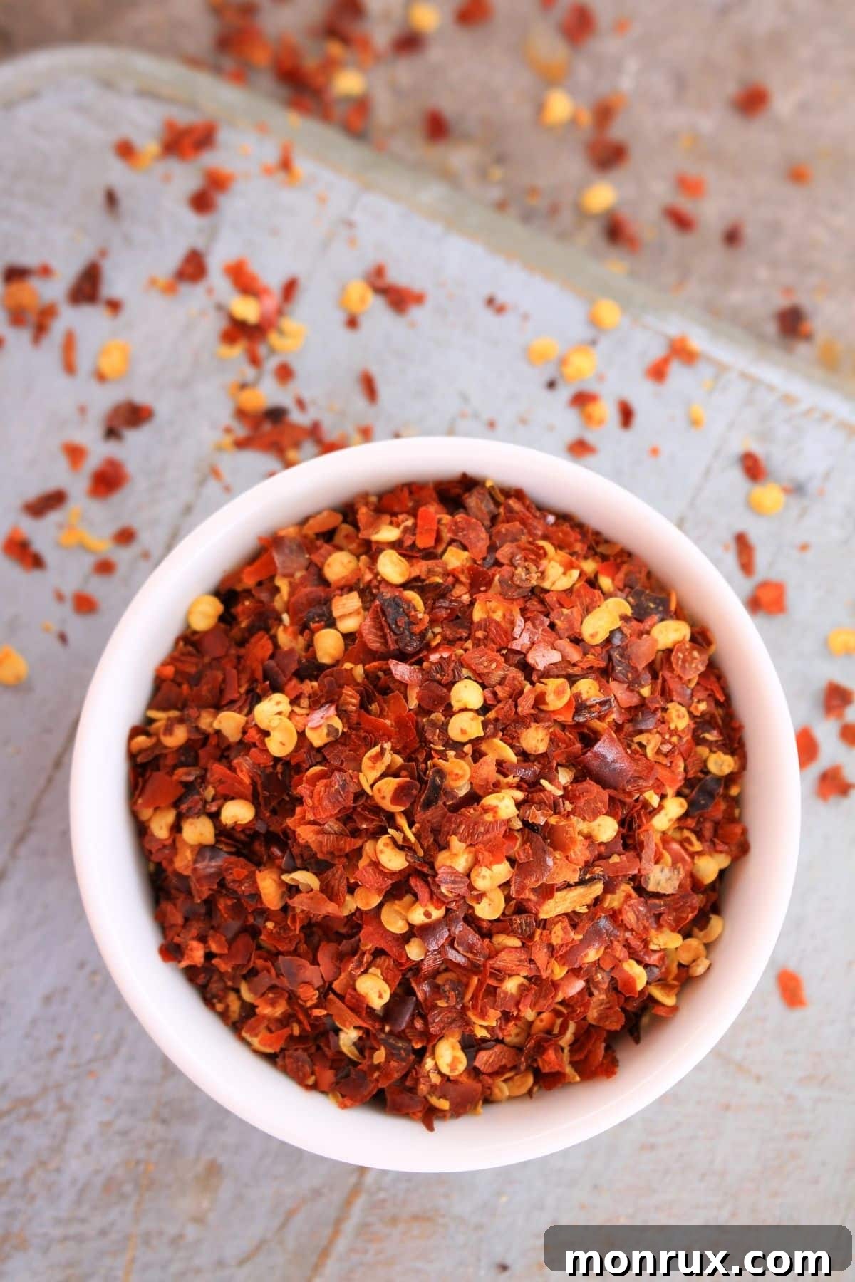 Bowl of red pepper flakes on wooden surface.
