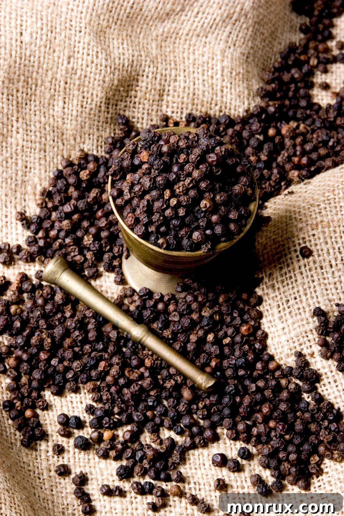 Bowl of dried black peppercorns on burlap surface.