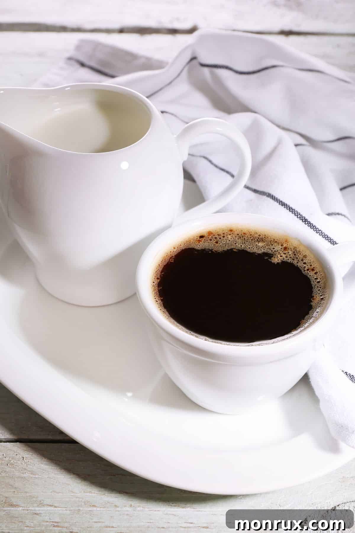 A steaming mug of coffee beside a small, elegant pitcher of creamer, set against a cozy backdrop.