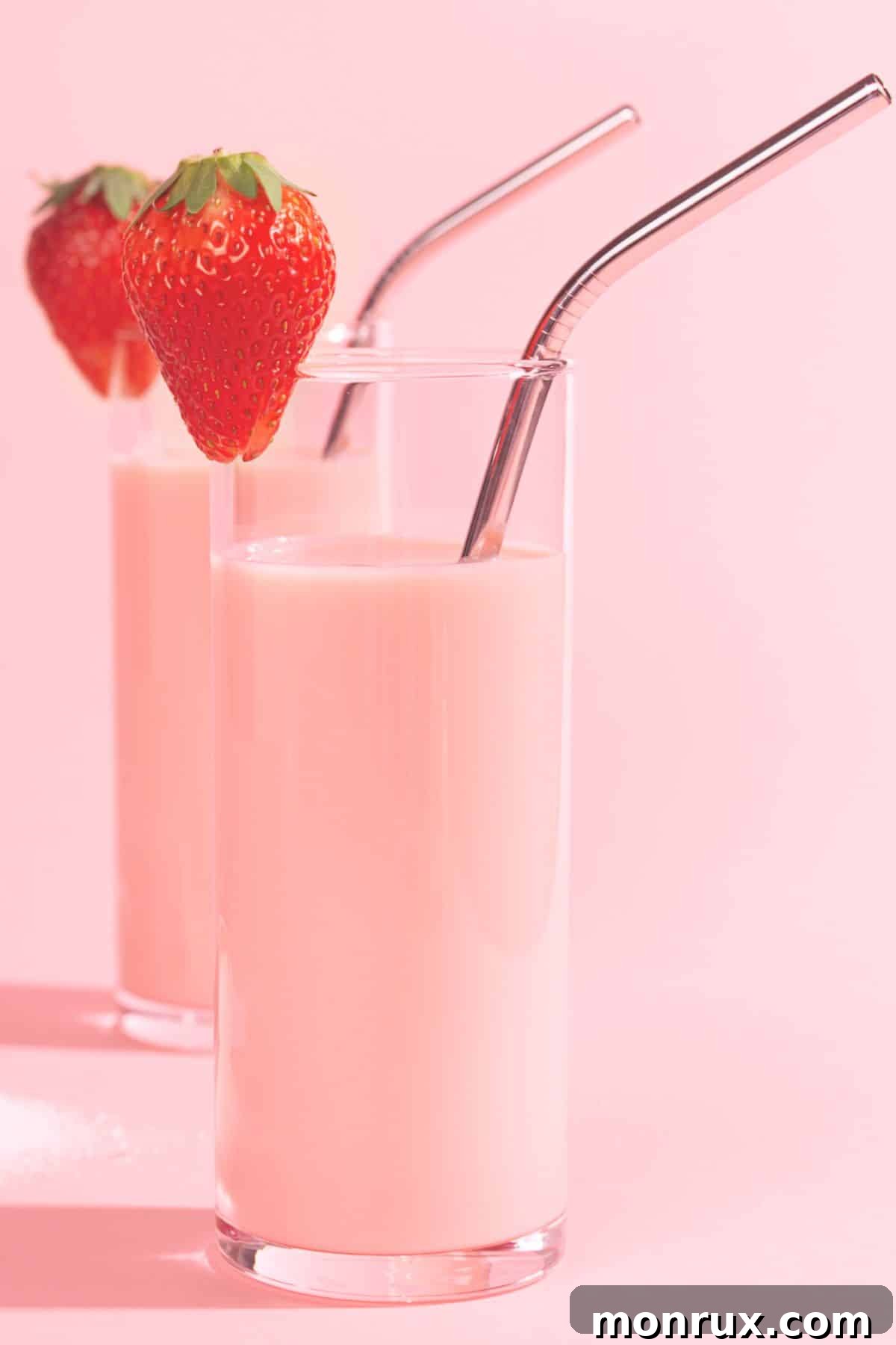 Two tall glasses of vibrant strawberry protein smoothies with elegant metal straws, showcasing a healthy and delicious beverage.