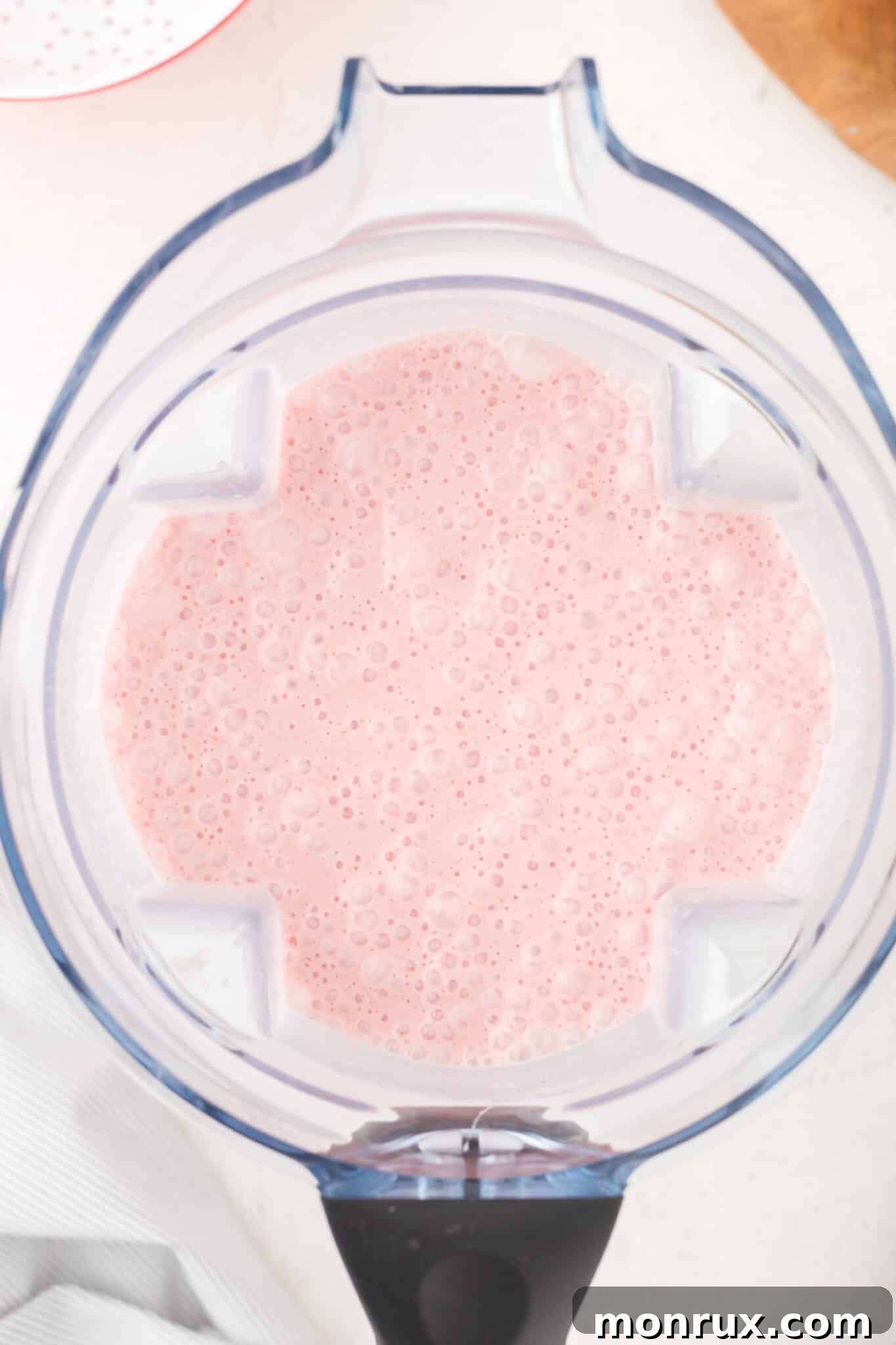 A vibrant strawberry smoothie swirls inside the jar of a high-speed blender, ready for blending.