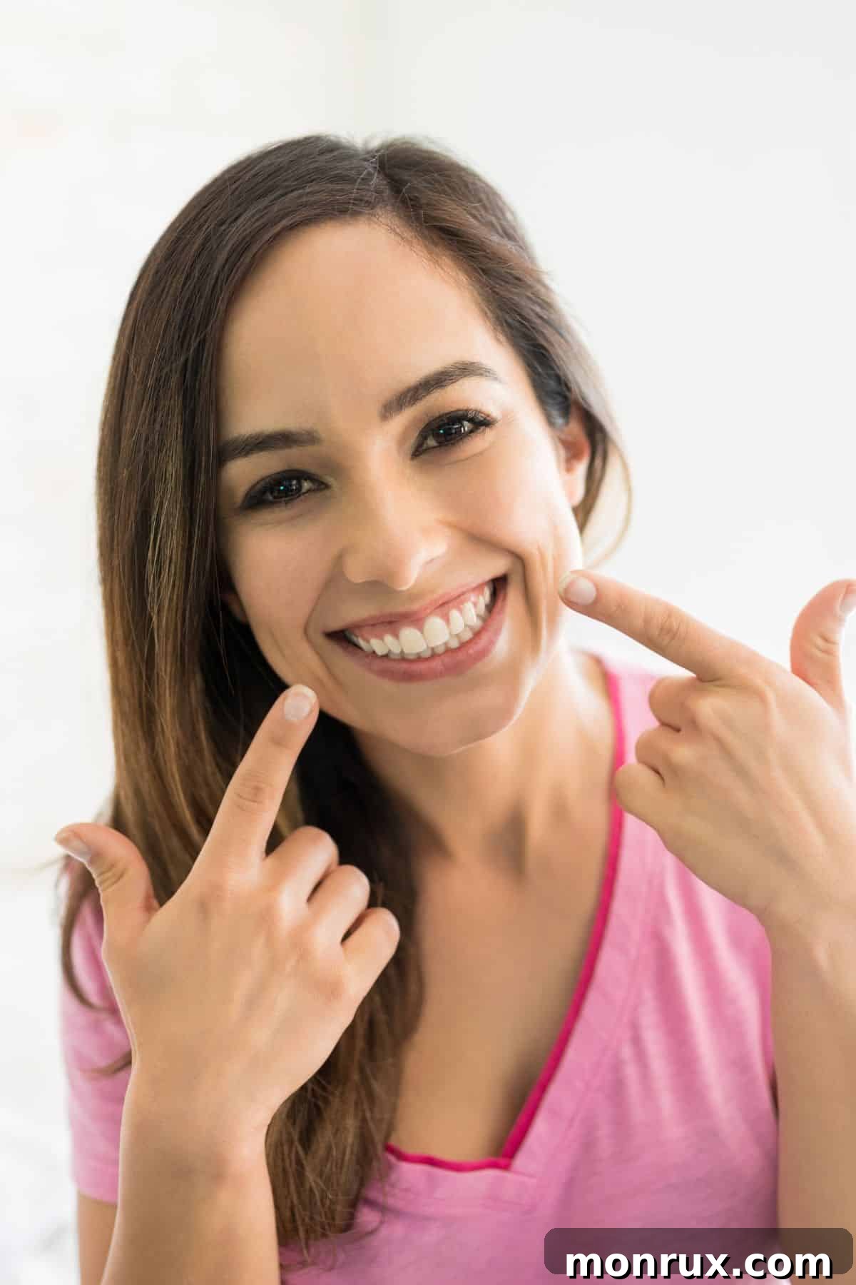 Brunette woman smiling, pointing to her healthy teeth with both index fingers, symbolizing good dental health through nutrition.