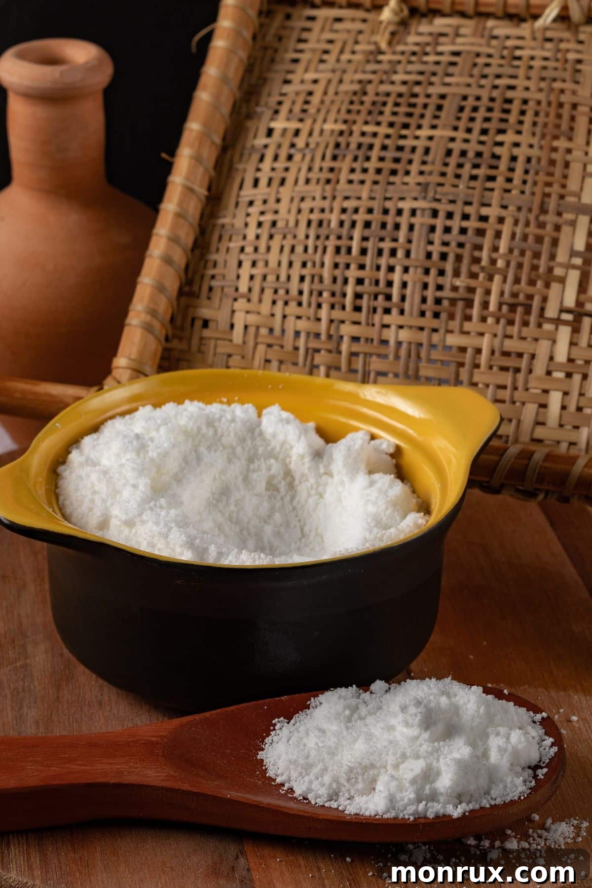 Bowl and spoonful of tapioca flour on wooden surface.