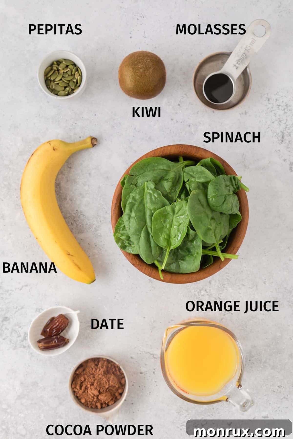 A selection of fresh ingredients laid out in small bowls on a white surface, including spinach, bananas, orange juice, blackstrap molasses, and cocoa powder, all ready to be blended into an iron-rich smoothie.