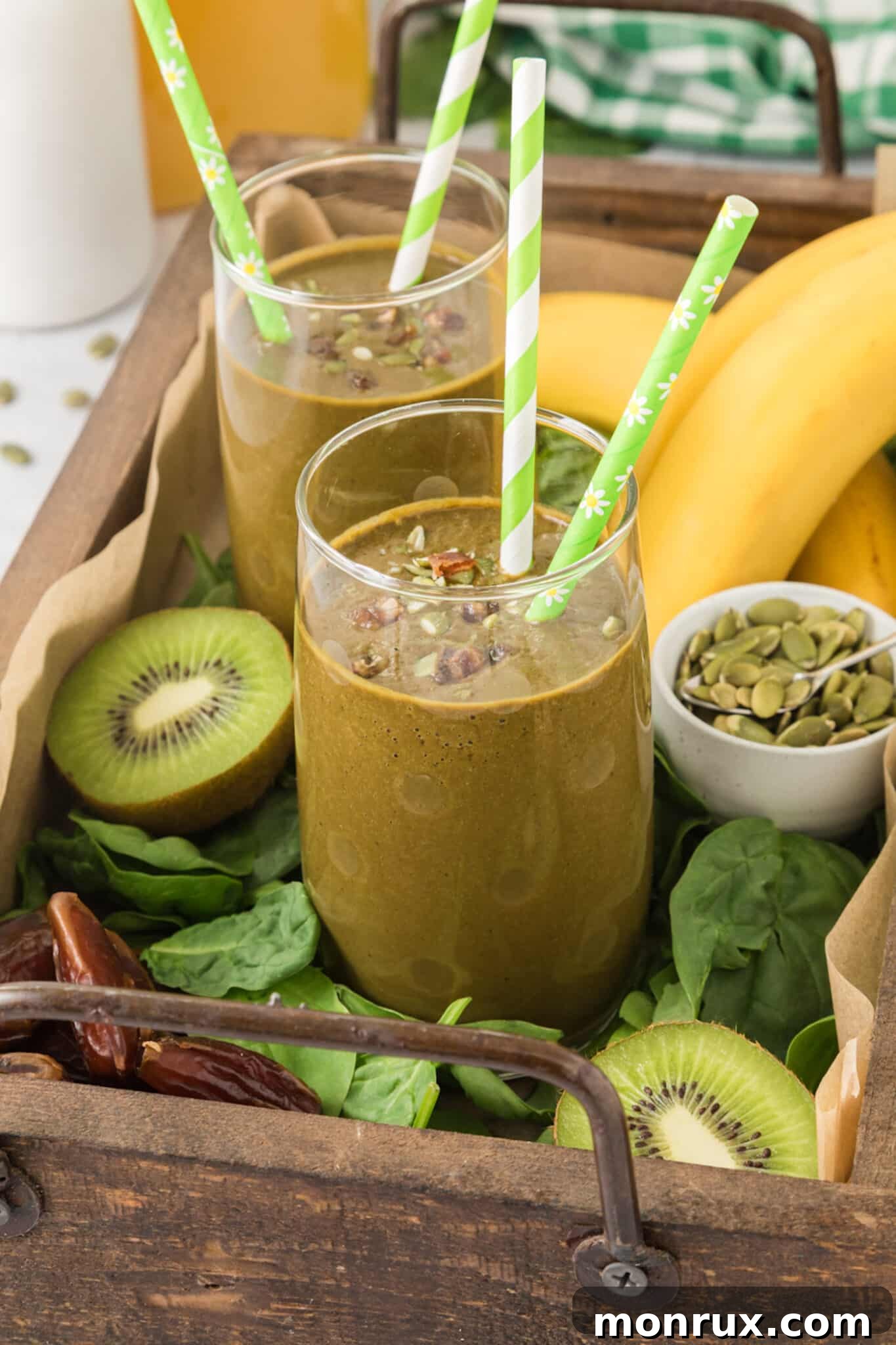 Two identical tall glasses of iron-rich green smoothie, each adorned with two cheerful green striped straws, reflecting a shared moment of healthy enjoyment.