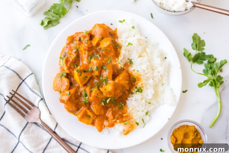 A white dinner plate loaded with white rice and chicken curry.