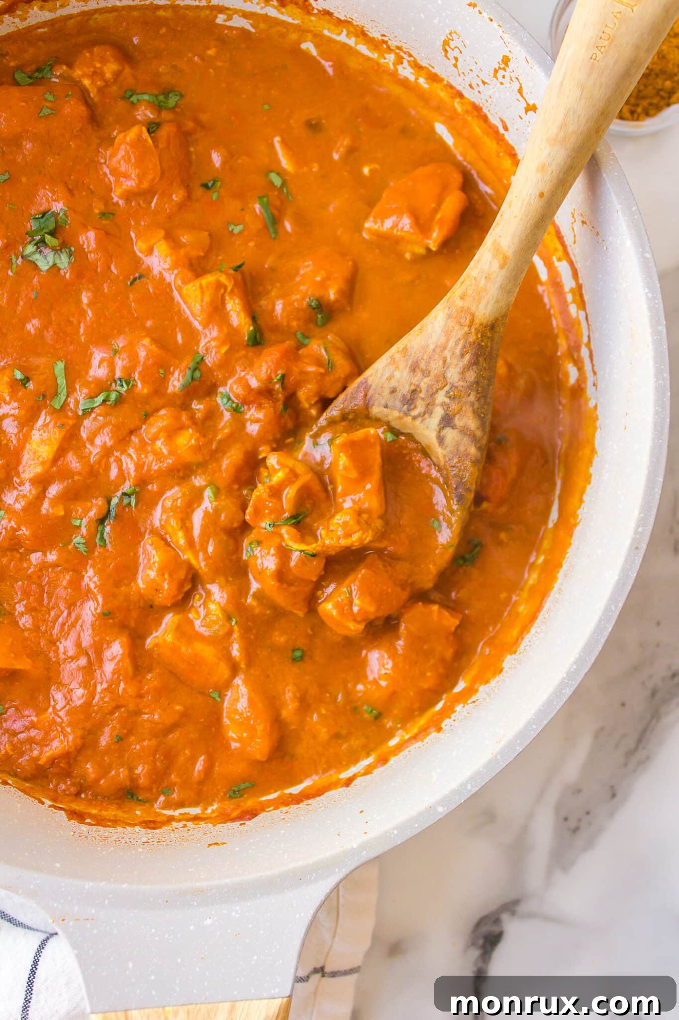 A wooden spoon resting in a bubbling saucepan of simple chicken curry, rich and inviting.