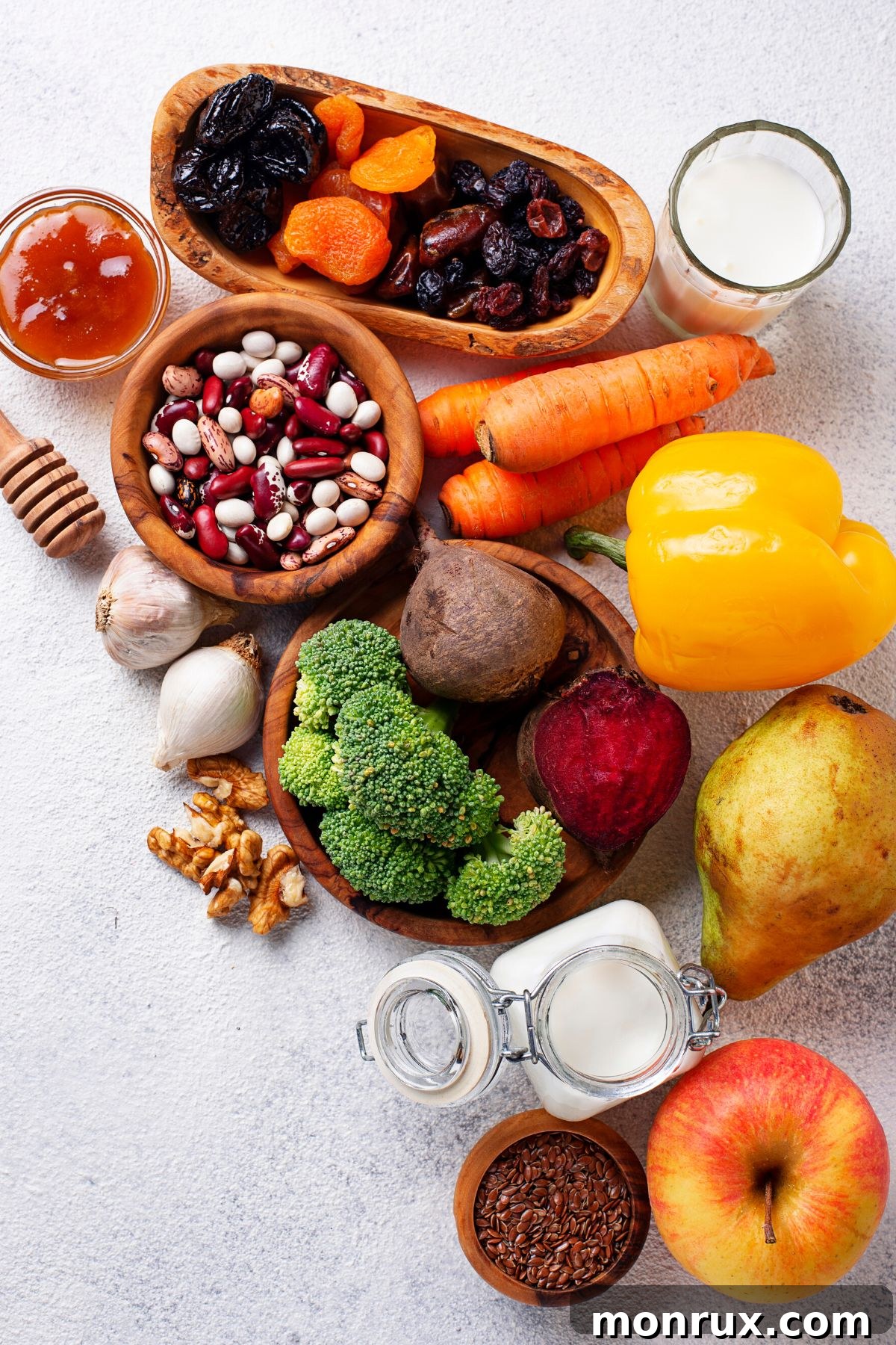 A vibrant selection of fresh produce, hearty dried beans, and golden honey laid out on a clean white surface, symbolizing wholesome gut health foods.