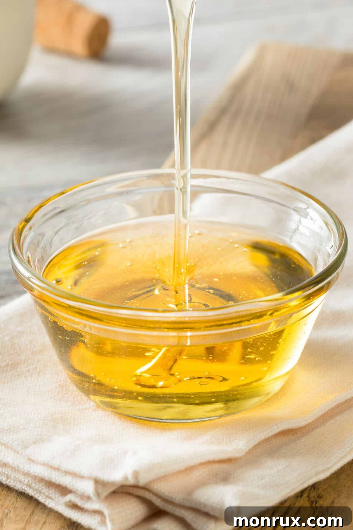 Agave nectar pouring into clear bowl on napkin and cutting board.