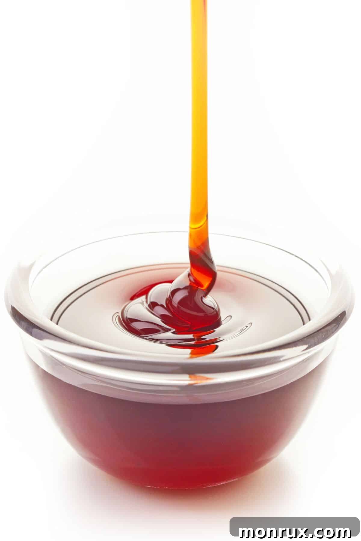 Brown rice syrup pouring into clear bowl on white background.
