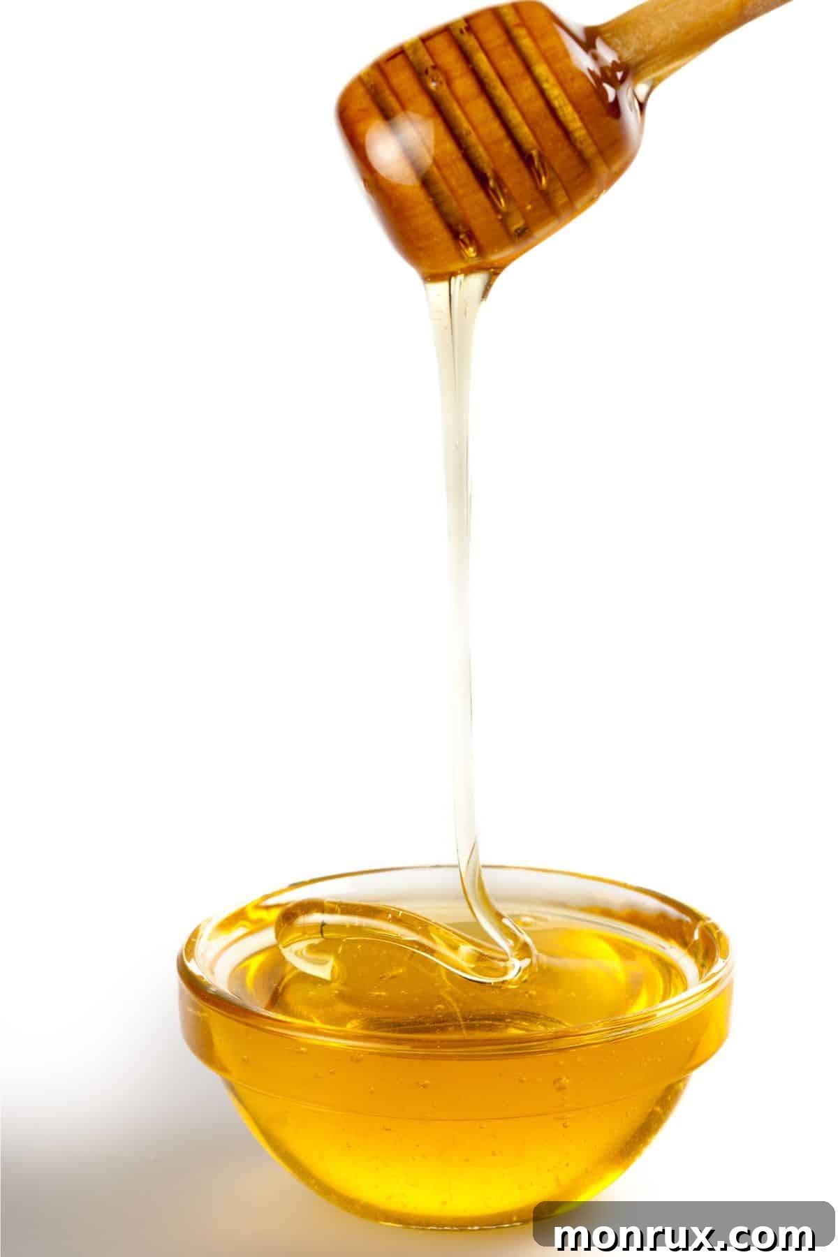 Honey pouring into clear bowl on white background.