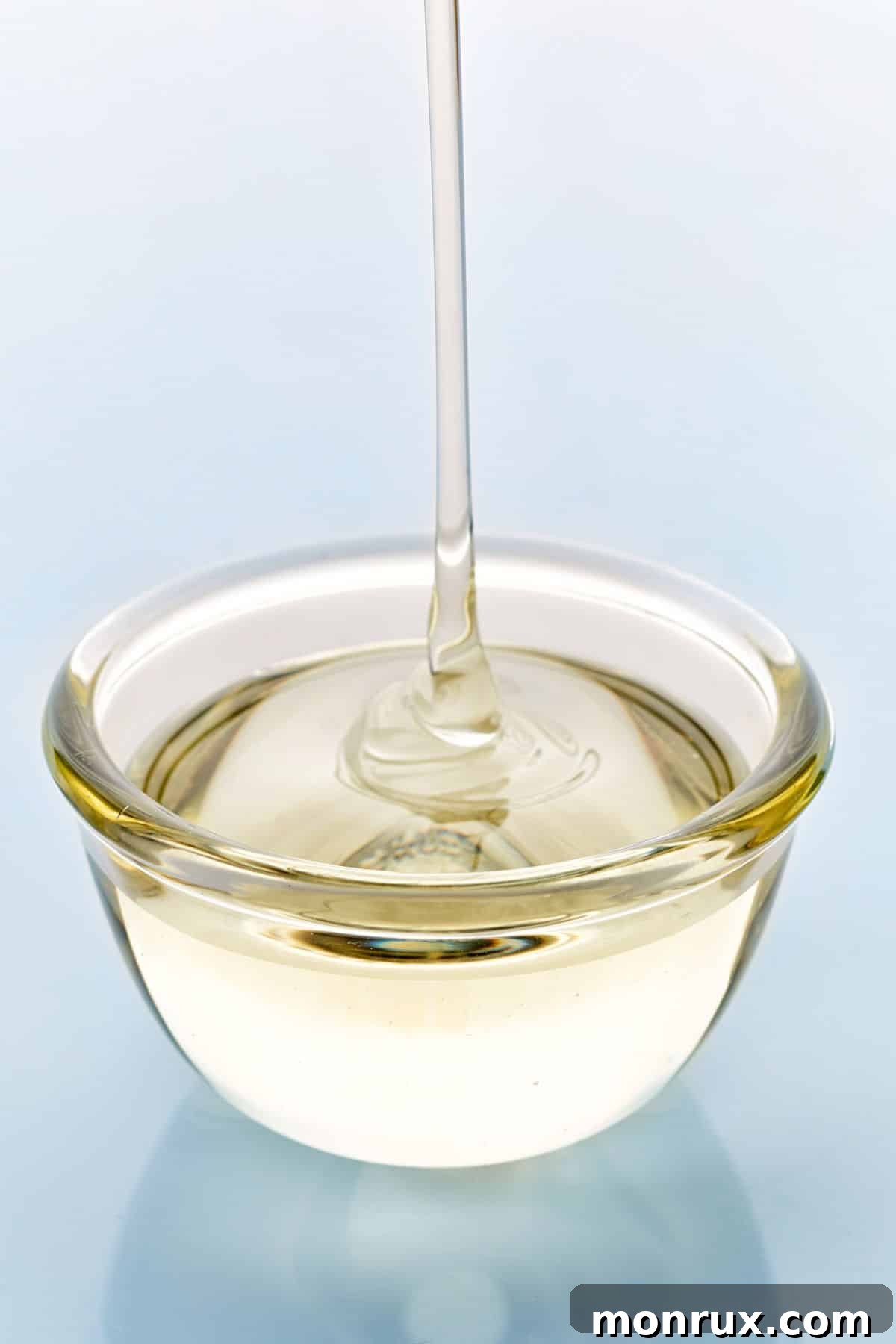 Light corn syrup pouring into clear bowl on light background.