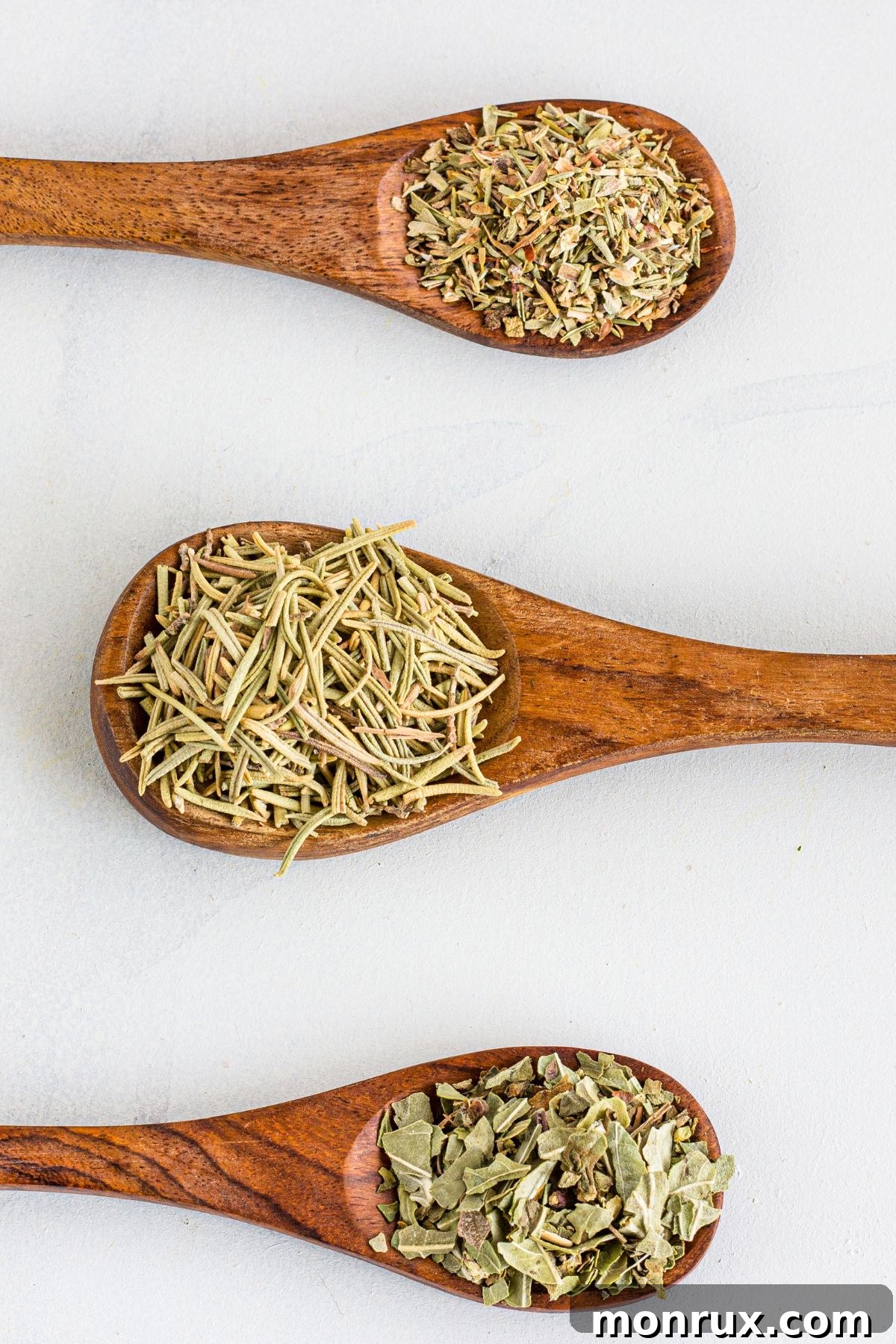 Spoons displaying individual dried herbs like oregano, rosemary, and thyme, essential components of Italian seasoning.