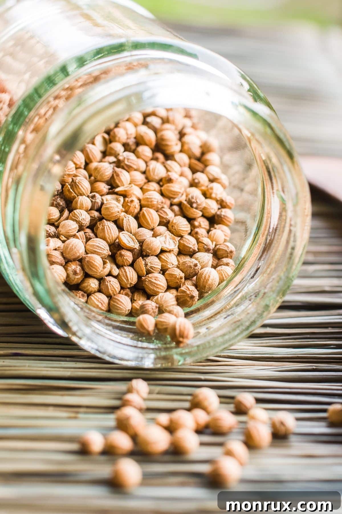 Glass jar spilling dried coriander seeds onto a wooden surface, indicating its potential as a dried basil substitute.
