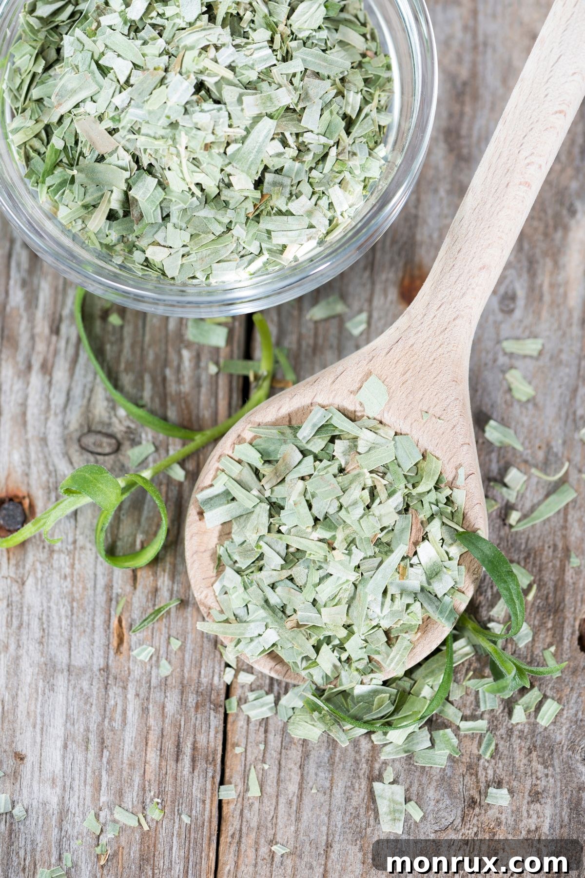 Bowl and spoon filled with dried tarragon on a wooden surface, presented as a dried basil alternative.