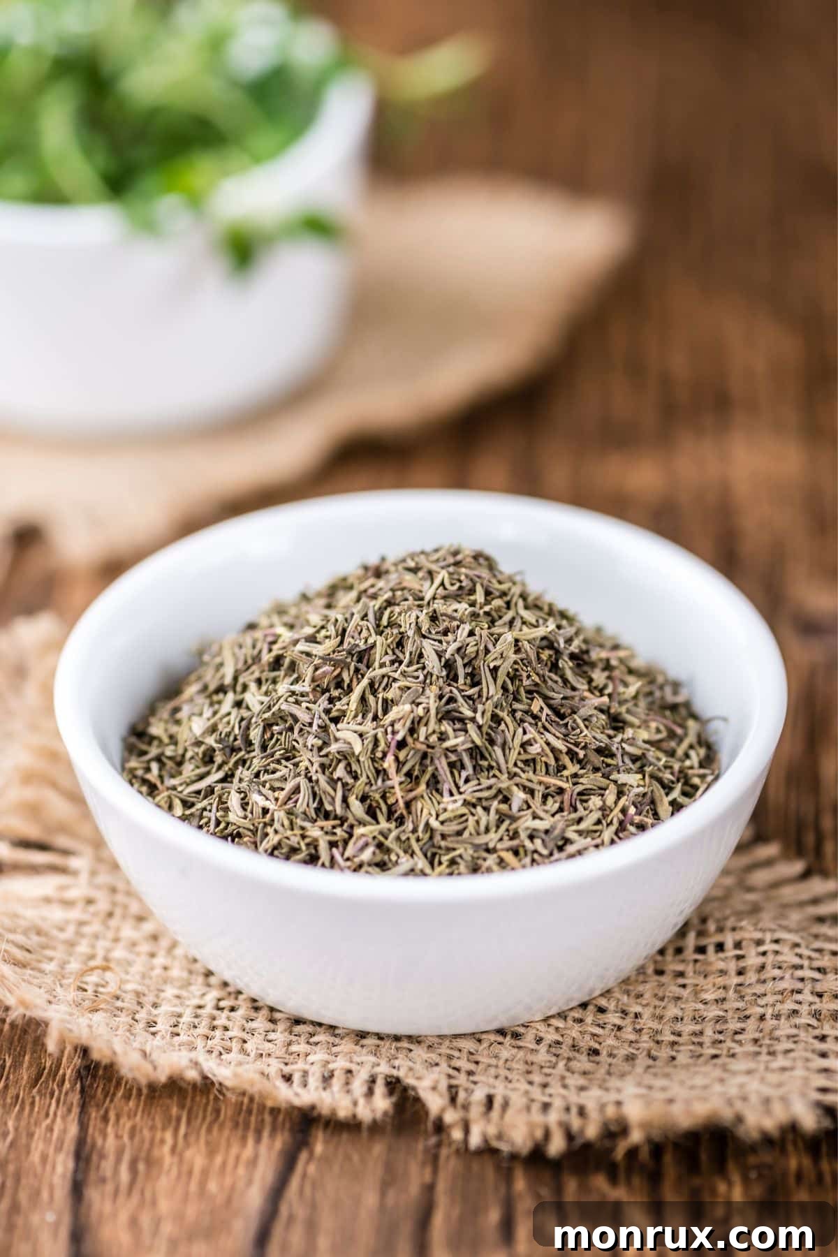 Bowl of dried thyme resting on burlap on a wooden surface, showcasing another substitute for dried basil.