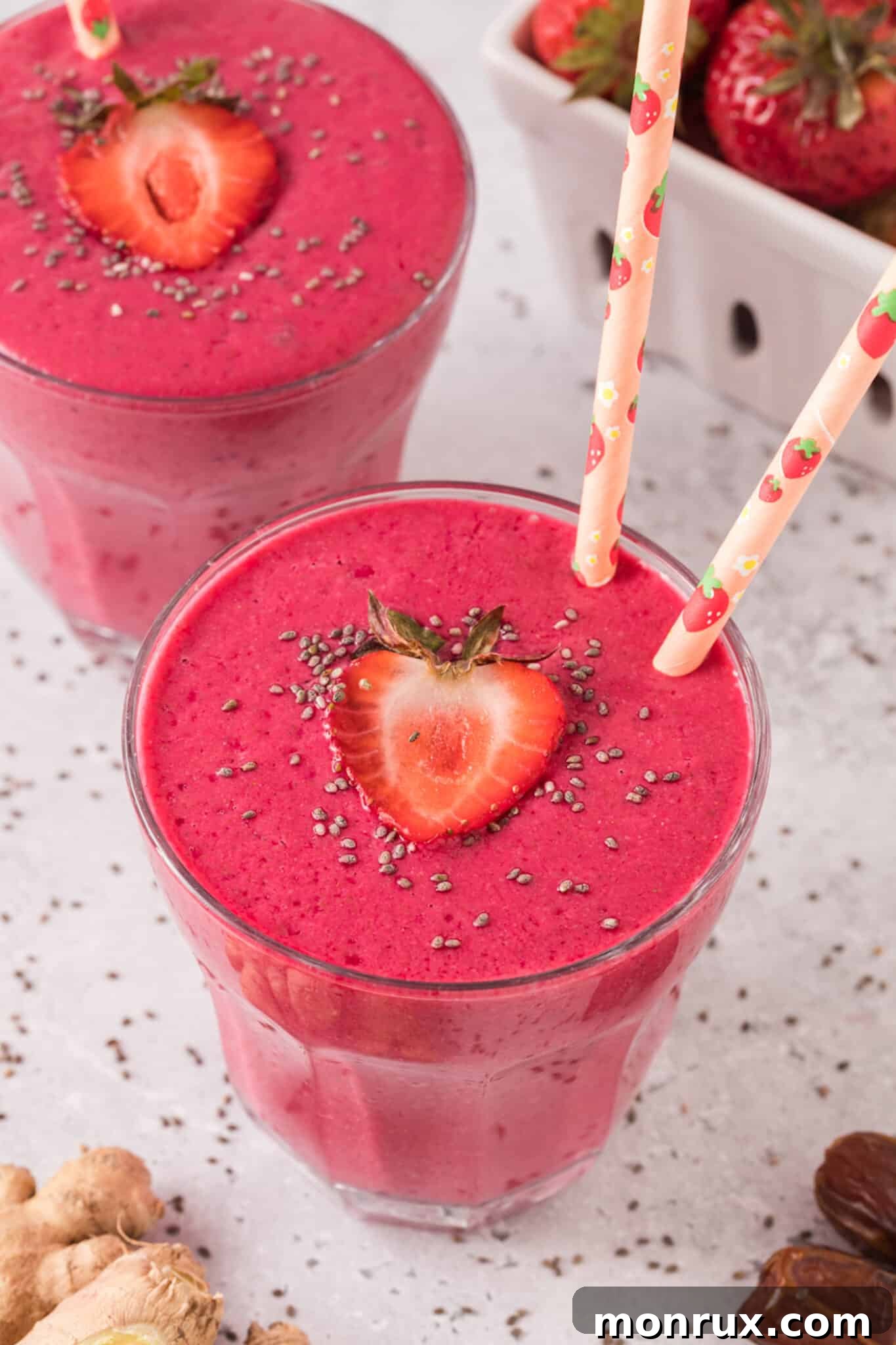 A vibrant pink strawberry beet smoothie in a glass with two pink straws, garnished with fresh strawberries and a sprinkle of chia seeds, promising natural constipation relief.