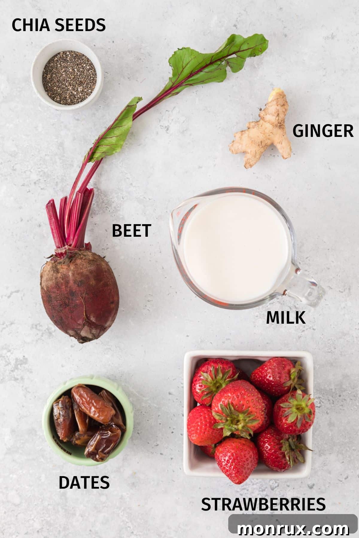 A selection of fresh ingredients laid out on a white surface, including cooked beets, strawberries, ginger, dates, and a container of almond milk, ready to make a strawberry beet constipation smoothie.