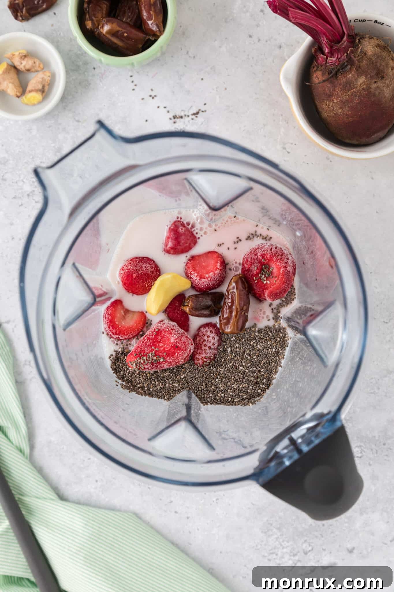 All the ingredients for the strawberry beet constipation smoothie, including milk, strawberries, beet, chia seeds, dates, and ginger, are neatly arranged inside a blender jar, ready to be processed into a smooth and healthy drink.
