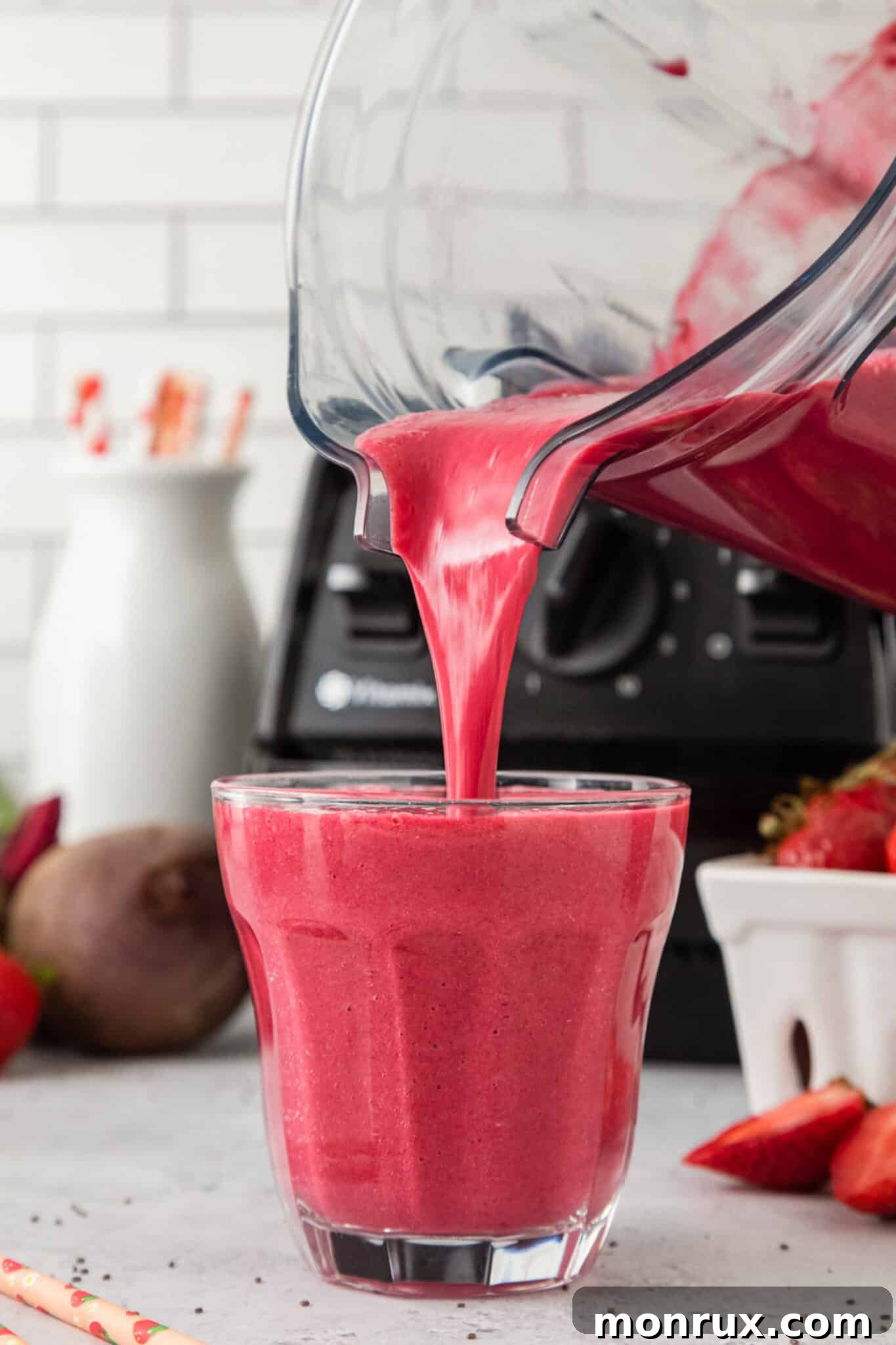 A stream of vibrant pink strawberry beet smoothie being poured from a high-speed blender jar into a clear glass, creating a refreshing and healthy drink.