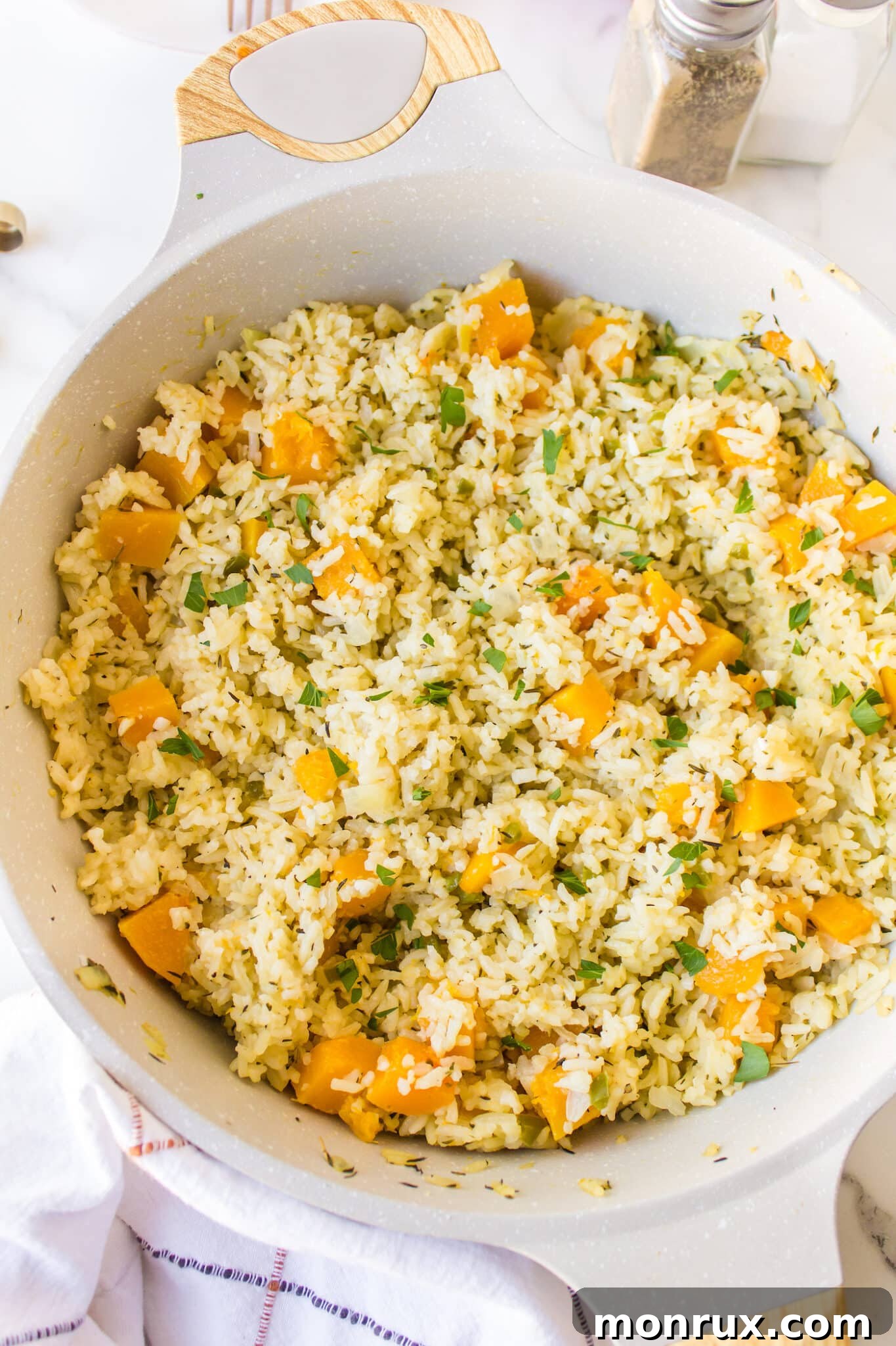 A white stockpot filled with cooked pumpkin rice, garnished with fresh herbs, ready to be served.