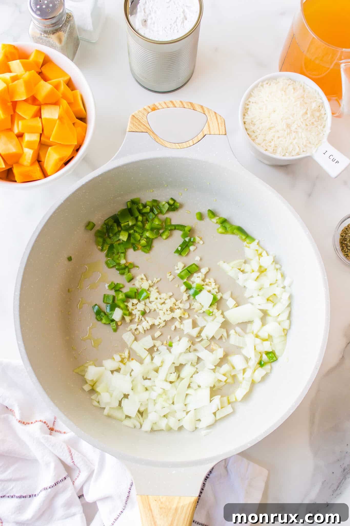 A large skillet showing chopped onions, garlic, and jalapeño pepper sizzling in oil, forming the aromatic base of the pumpkin rice.