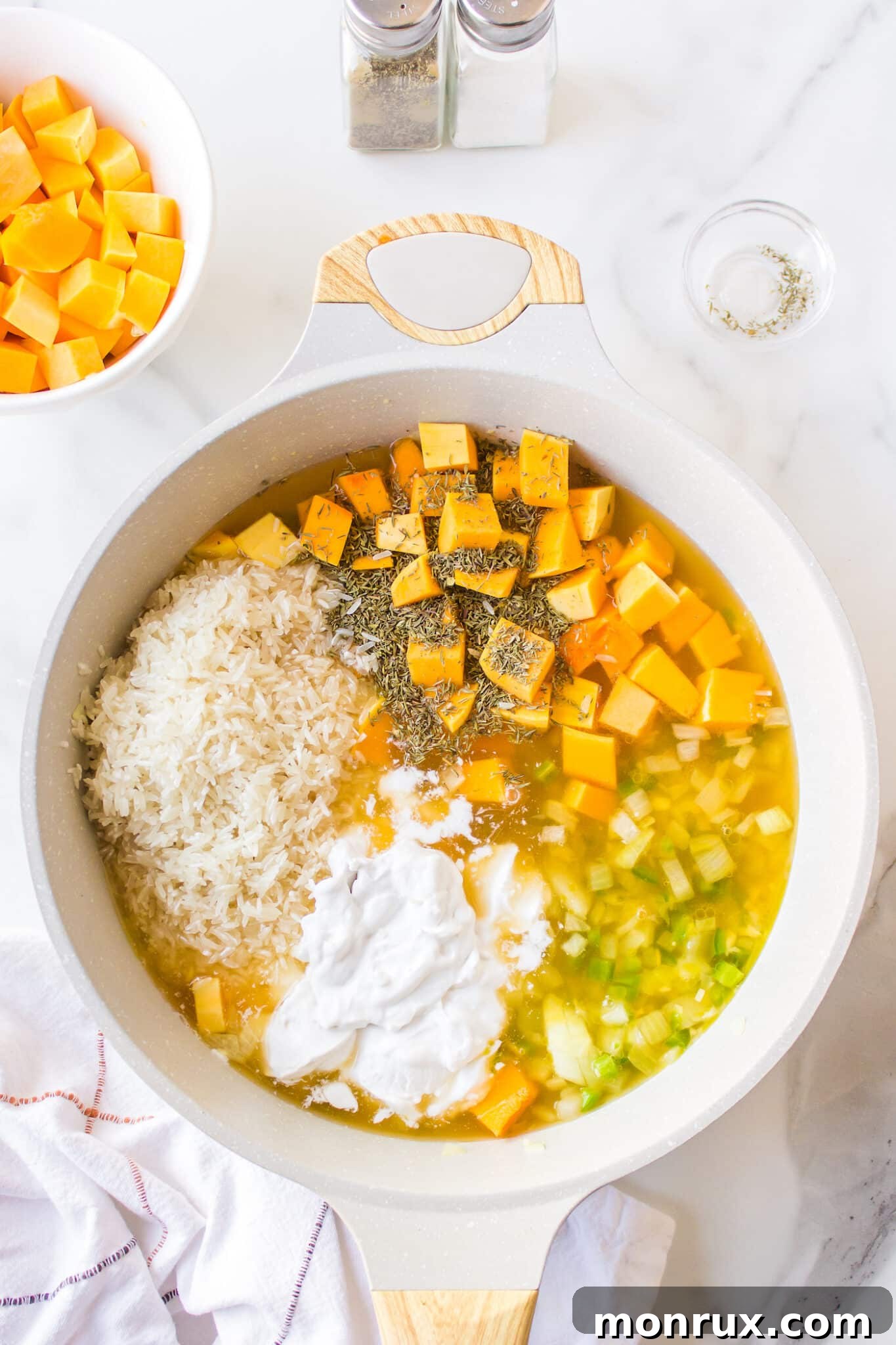 All ingredients for pumpkin rice, including rice, chopped pumpkin, coconut milk, and vegetable broth, combined in the skillet and ready to cook.