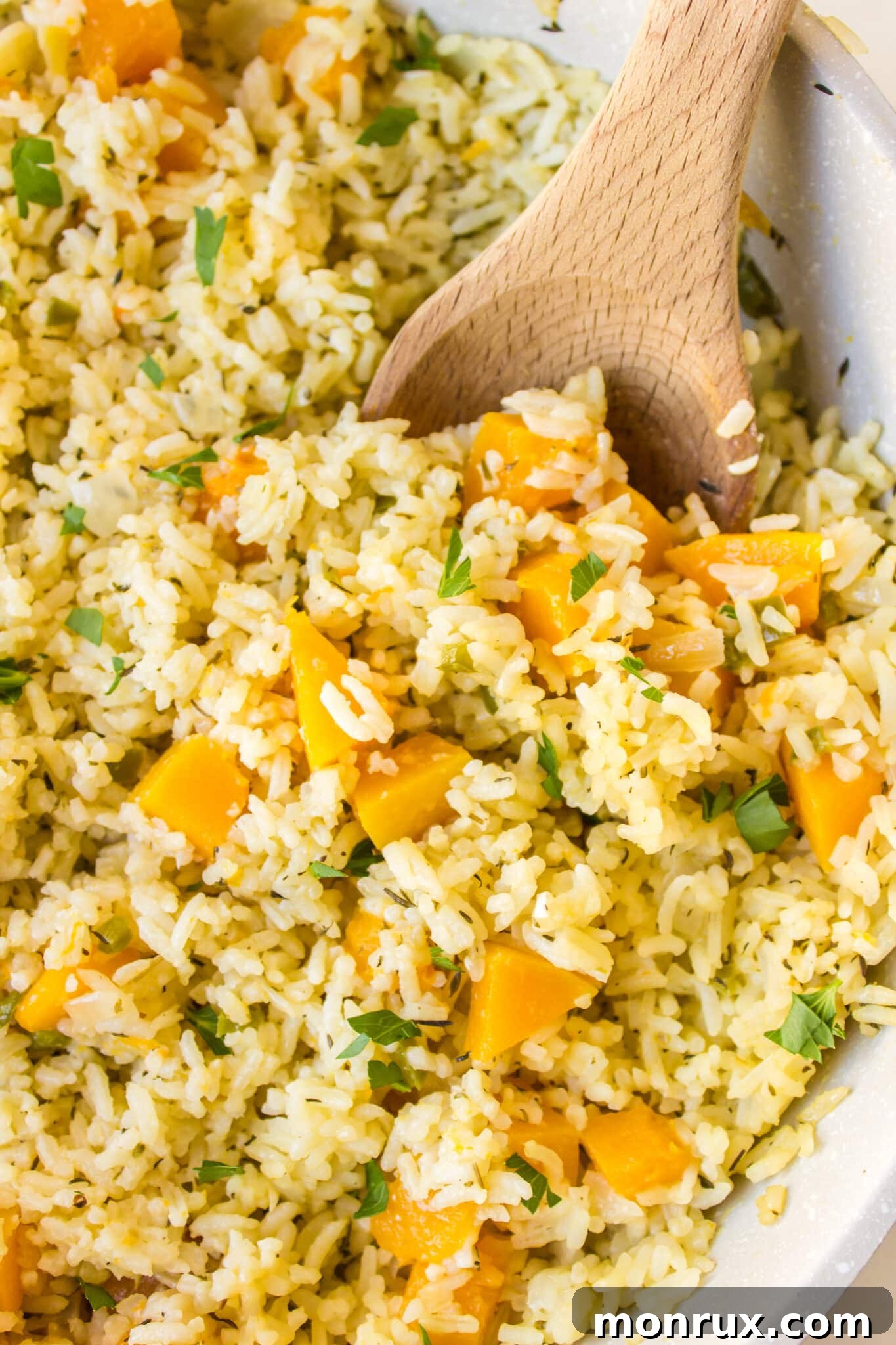 A wooden spoon gently fluffing the fully cooked pumpkin rice in the pan, showcasing its fluffy texture and golden color.