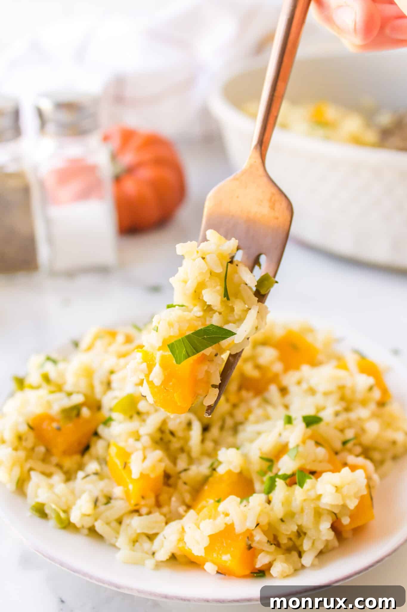 A forkful of savory pumpkin rice lifted from a small, elegant serving on a white plate, highlighting its creamy texture.