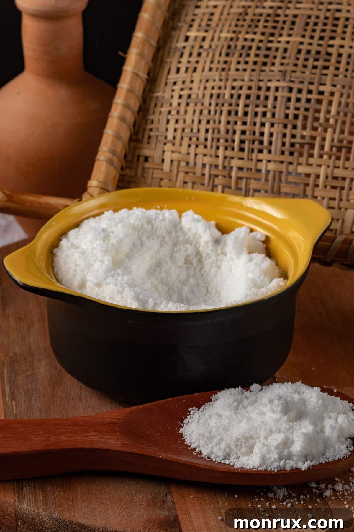 Bowl and spoonful of bright white tapioca flour on a rustic wooden surface, showcasing its fine, starchy texture.