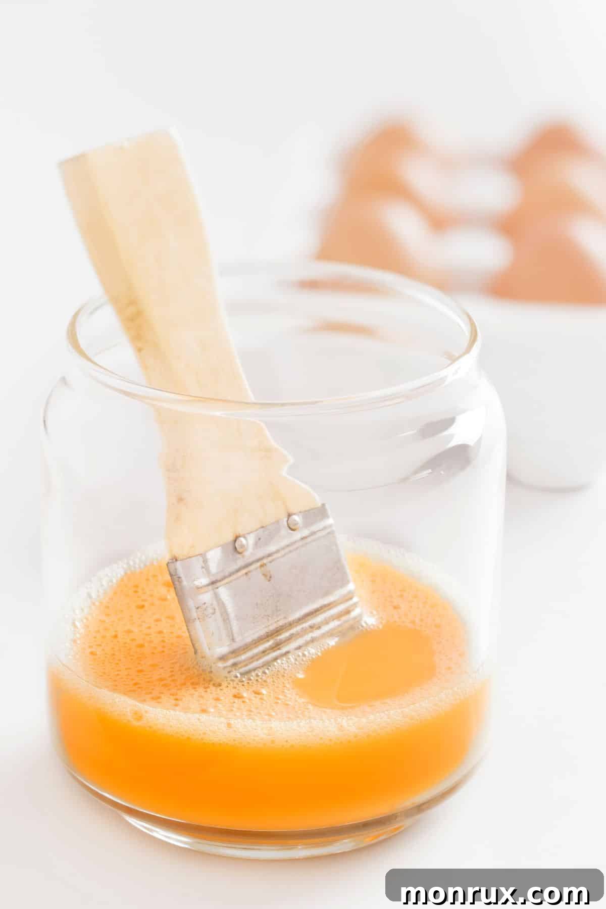 Clear glass of egg wash with brush.