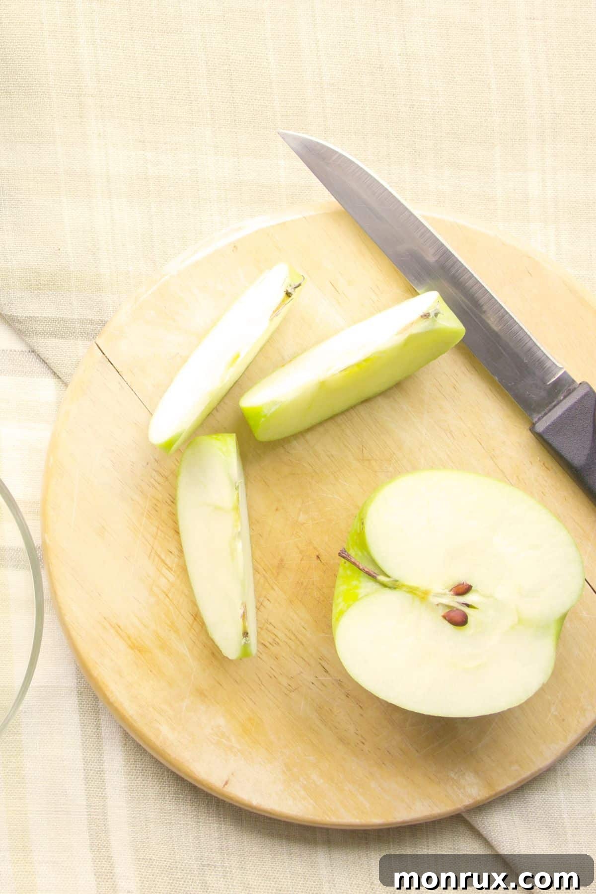 Halved and sliced green apple on wooden cutting board.