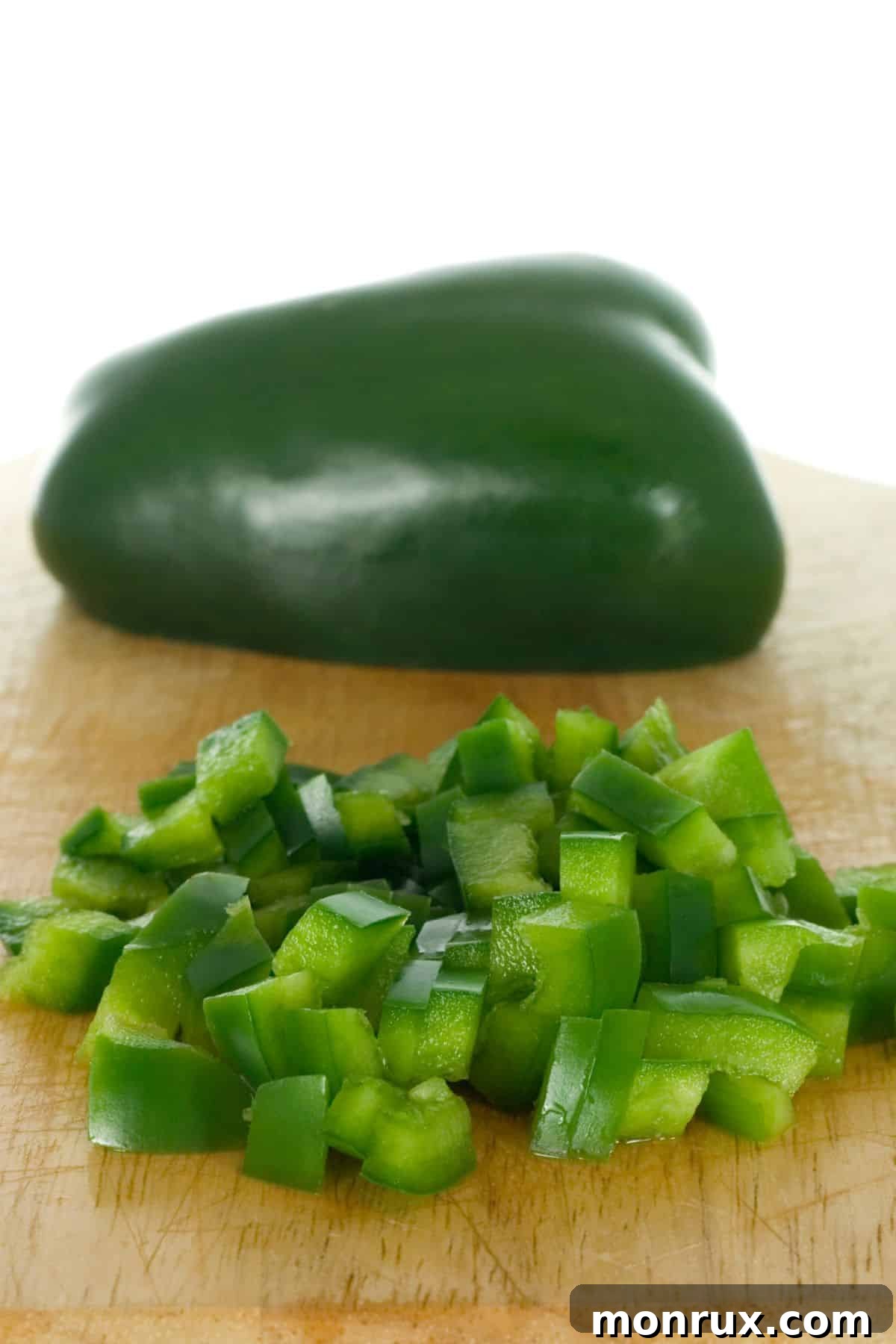 Halved and chopped green pepper on wooden cutting board.