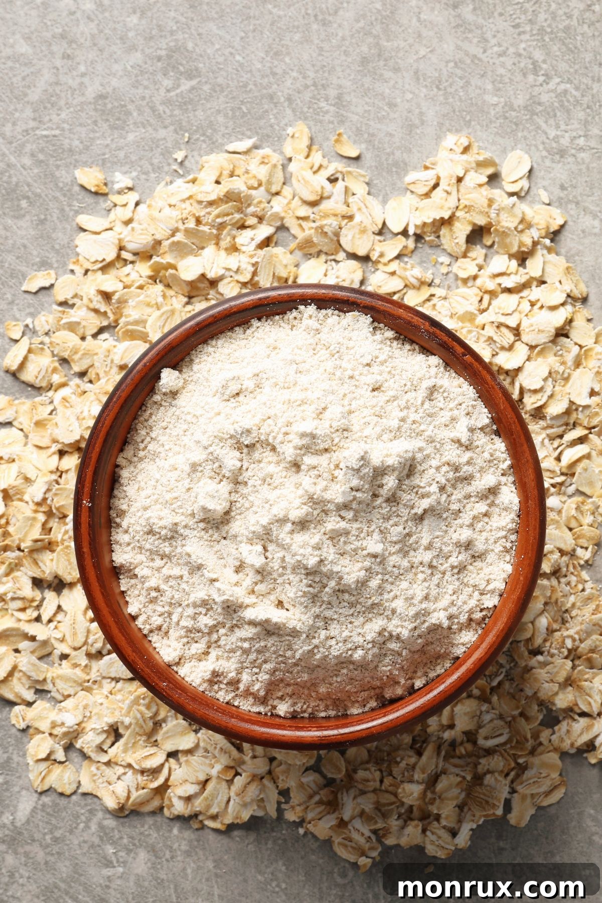 A rustic bowl filled with finely ground oat flour, surrounded by scattered whole rolled oats on a textured stone surface, highlighting the transformation from whole grain to versatile baking ingredient.