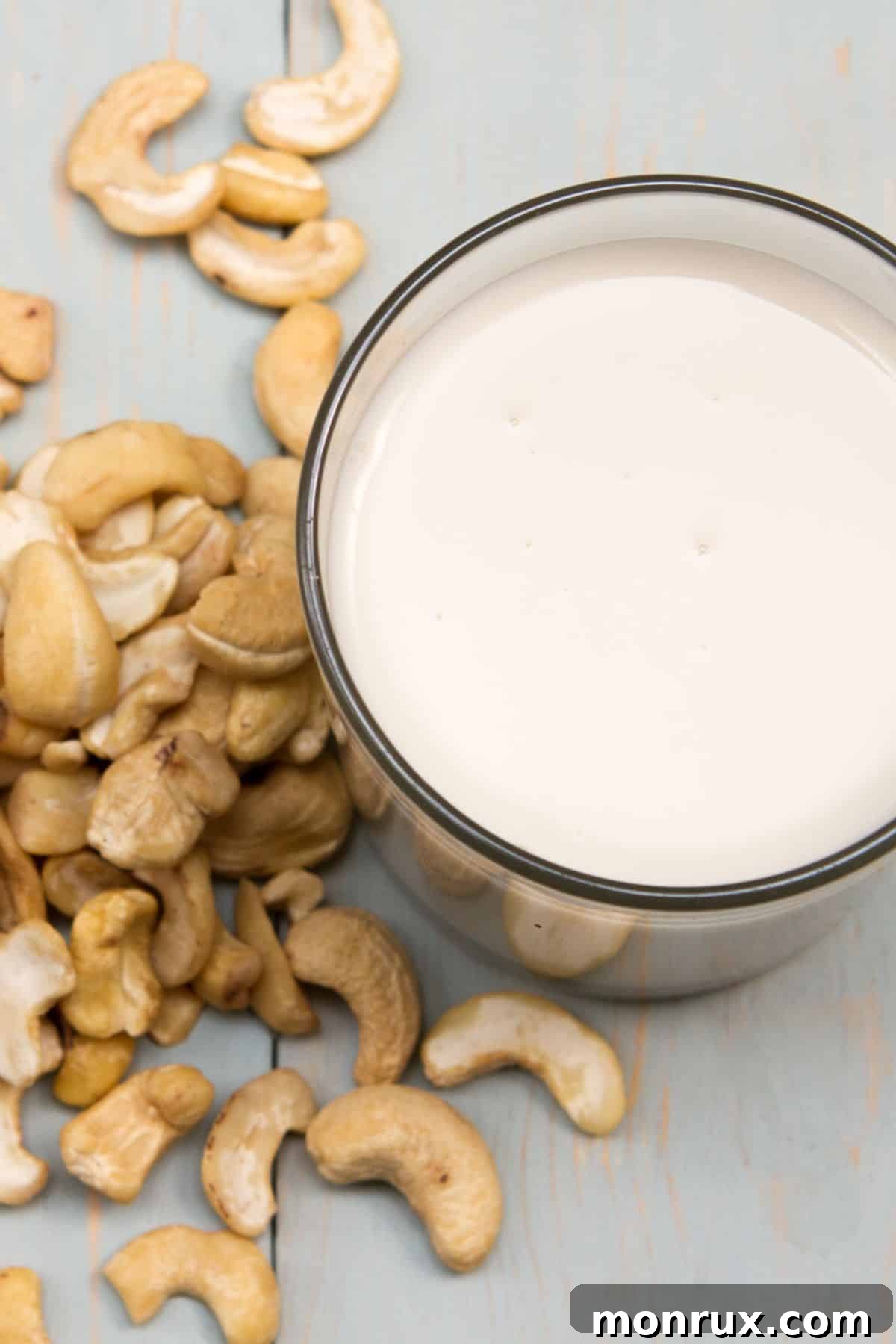 a glass of cashew cream surrounded by cashews on a table.