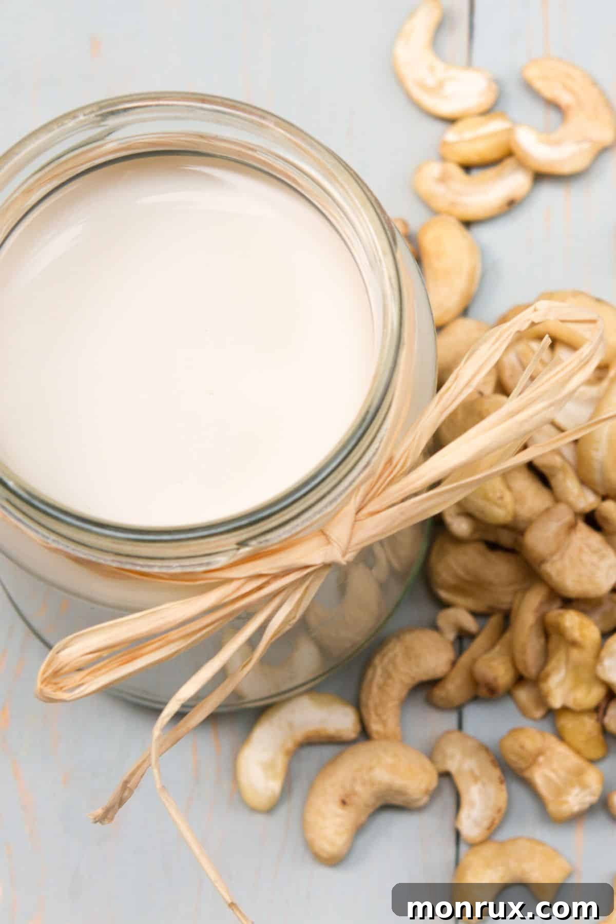 a glass of cashew cream next to cashews on a table.